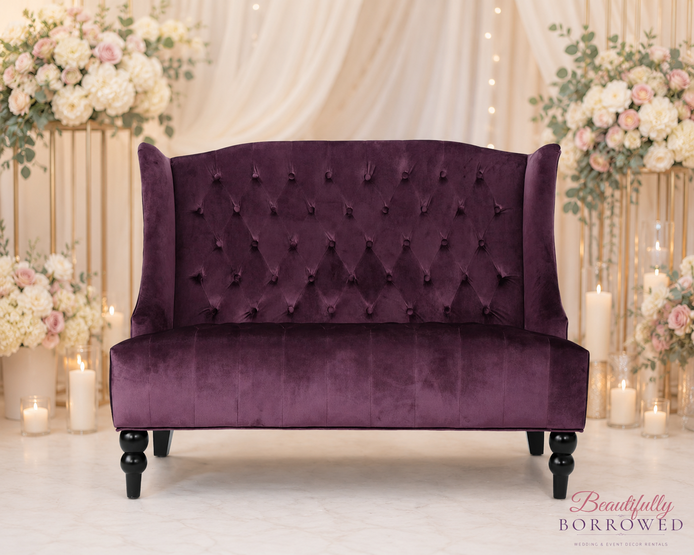 A purple tufted loveseat with dark wooden legs in front of a wedding backdrop with floral arrangements and candles.