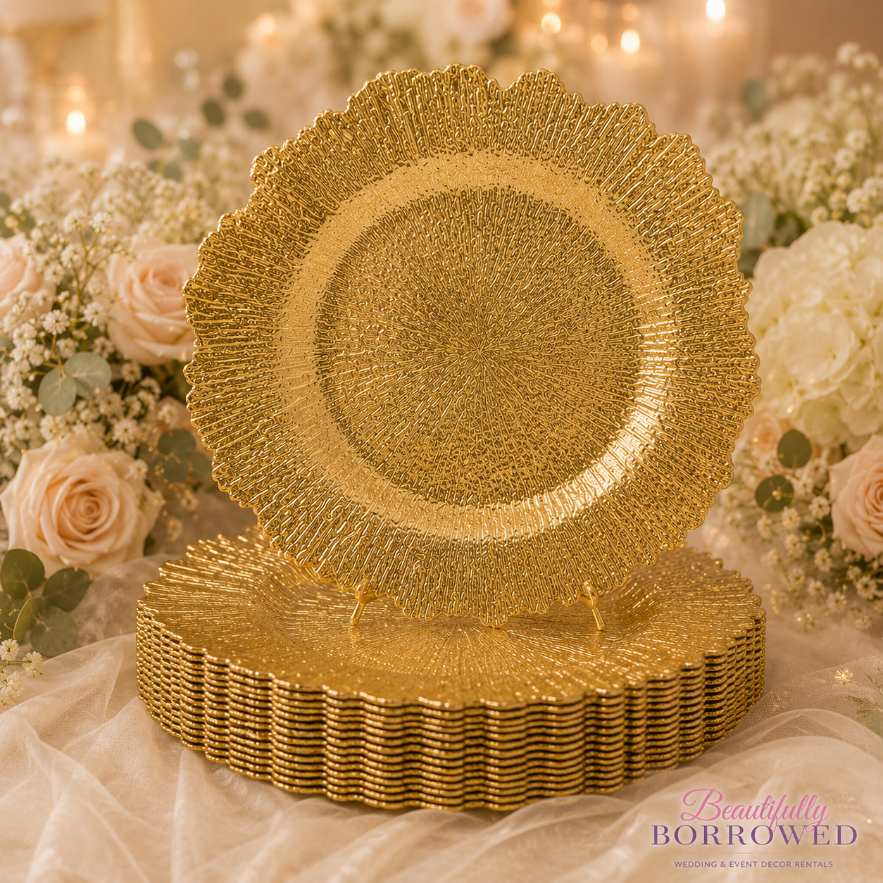 A stack of decorative gold plates with intricate designs, surrounded by a floral arrangement of cream roses, baby's breath, and greenery, on a soft fabric surface.