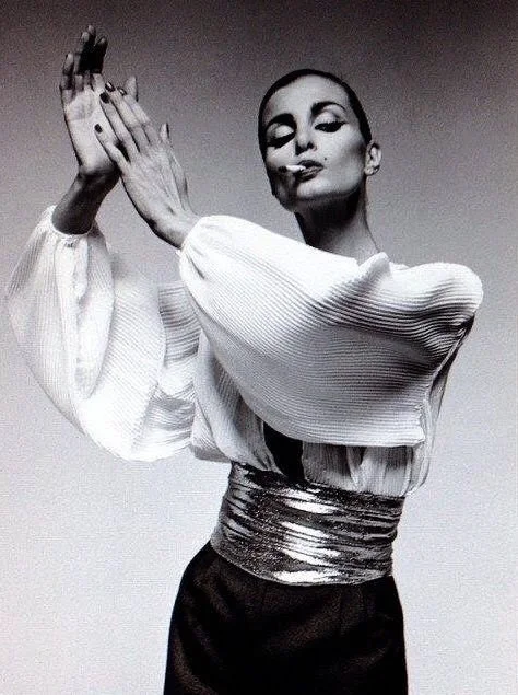 A woman in stylish clothing posing with her hands raised near her face in black and white photo.