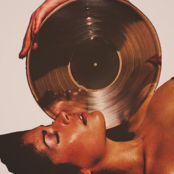 A woman lying down with her eyes closed, holding a large vinyl record close to her face.