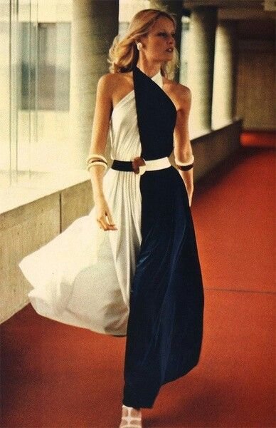 Woman in a stylish black and white dress walking along a corridor with large glass windows.