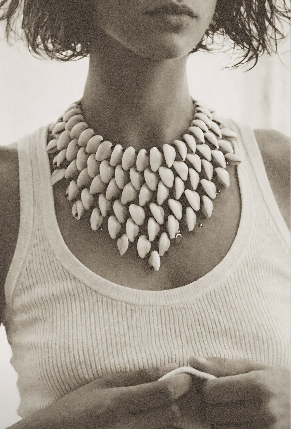 A person wearing a sleeveless top and a layered ocean shell necklace with white shells.