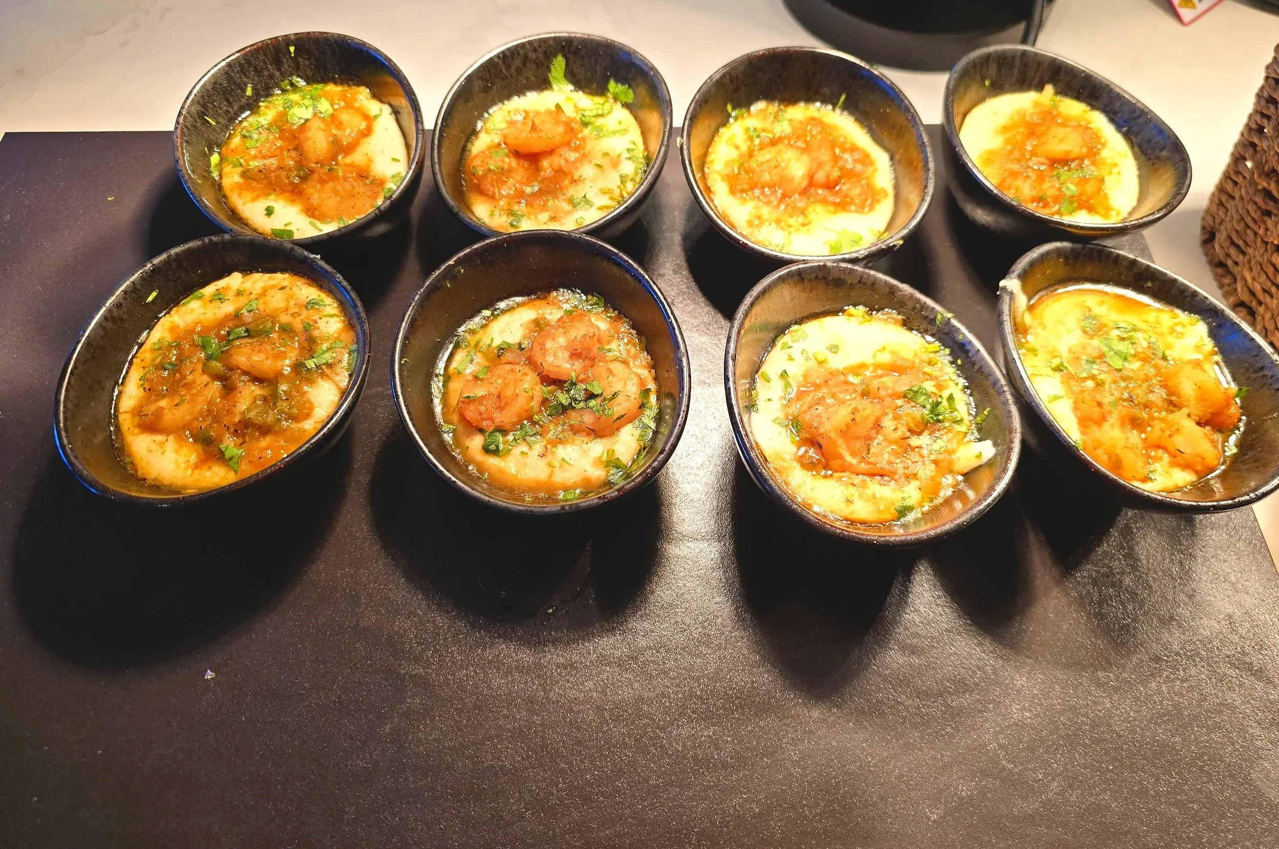 Eight small black bowls filled with a yellow-colored curry topped with fresh cilantro and garnished with ginger and green chili.