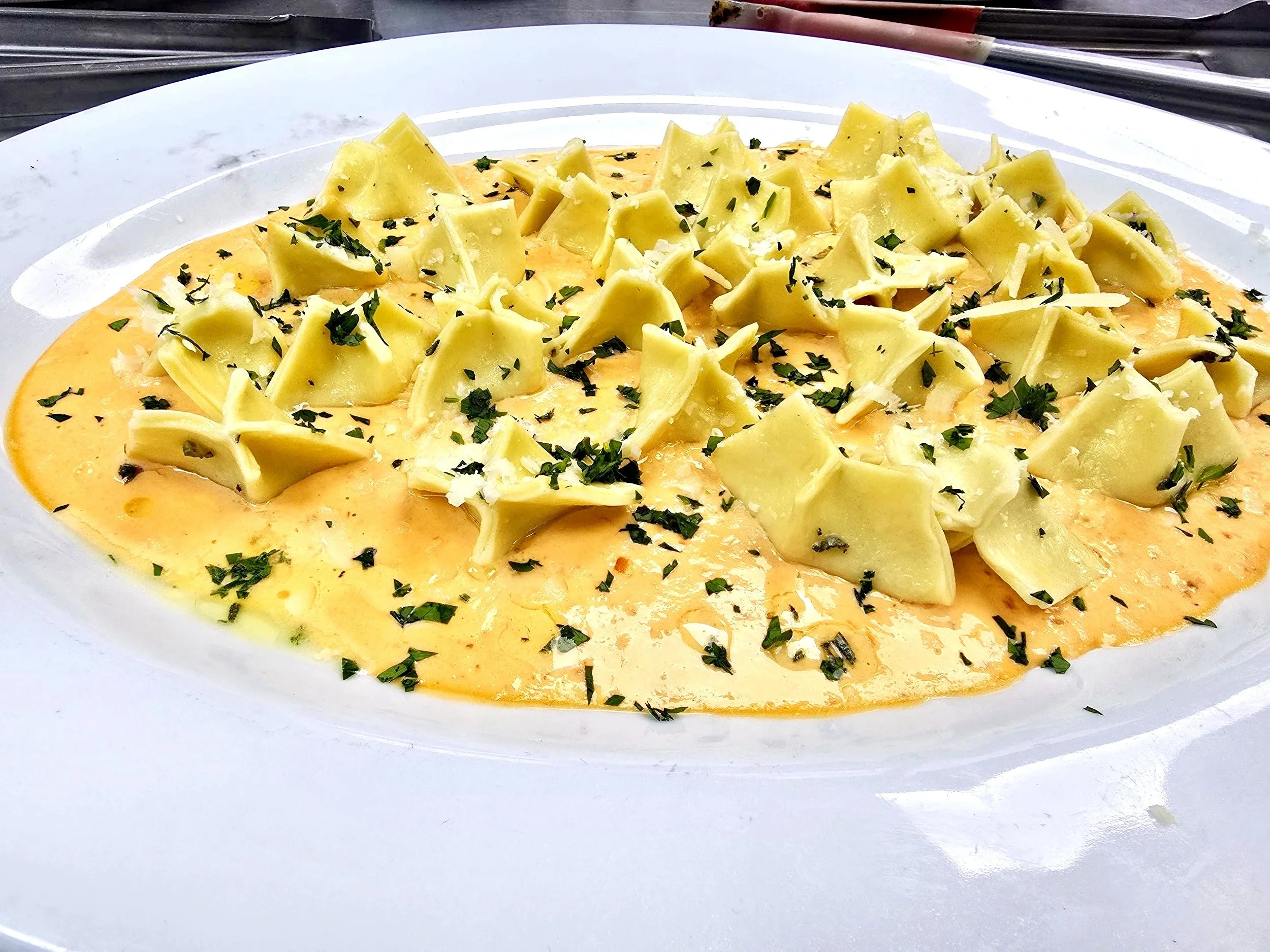 A white plate of creamy, yellow cheese dip topped with chopped herbs and chunks of cheese.