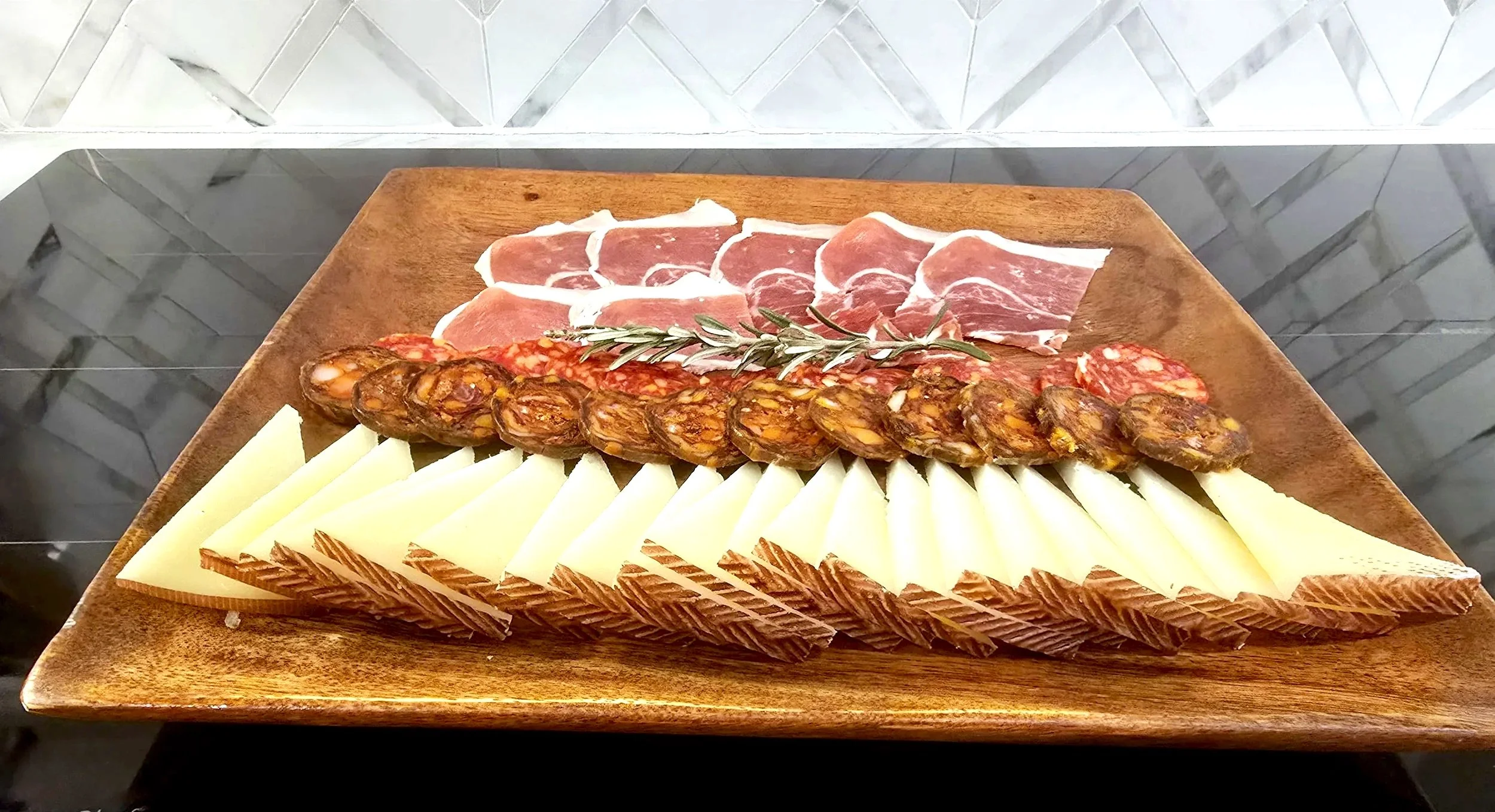 Charcuterie board with slices of cheese, salami, prosciutto, chorizo, and topped with a sprig of rosemary