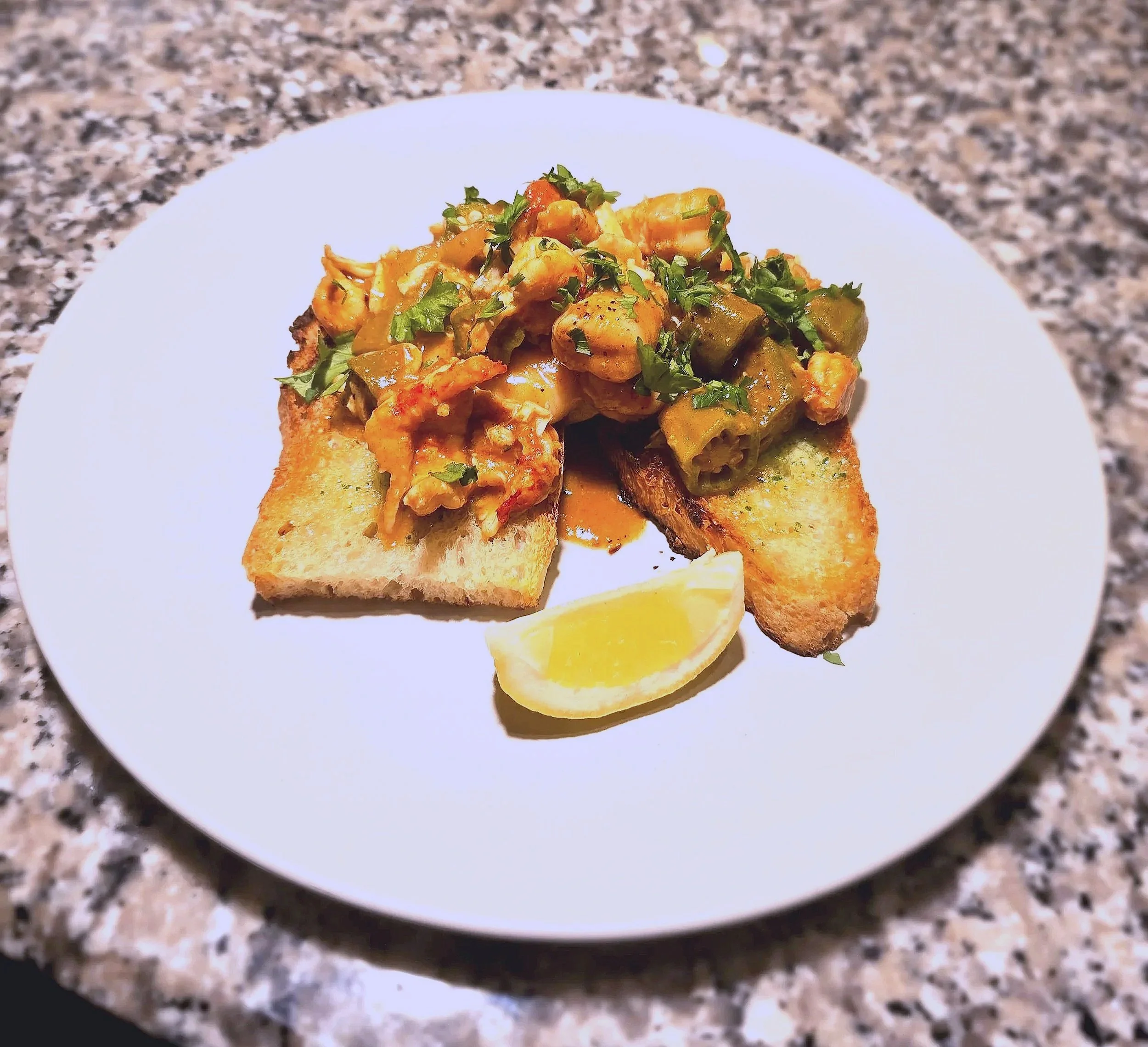 A plate of avocado toast topped with seasoned chicken pieces, chopped herbs, and a lemon wedge on the side.