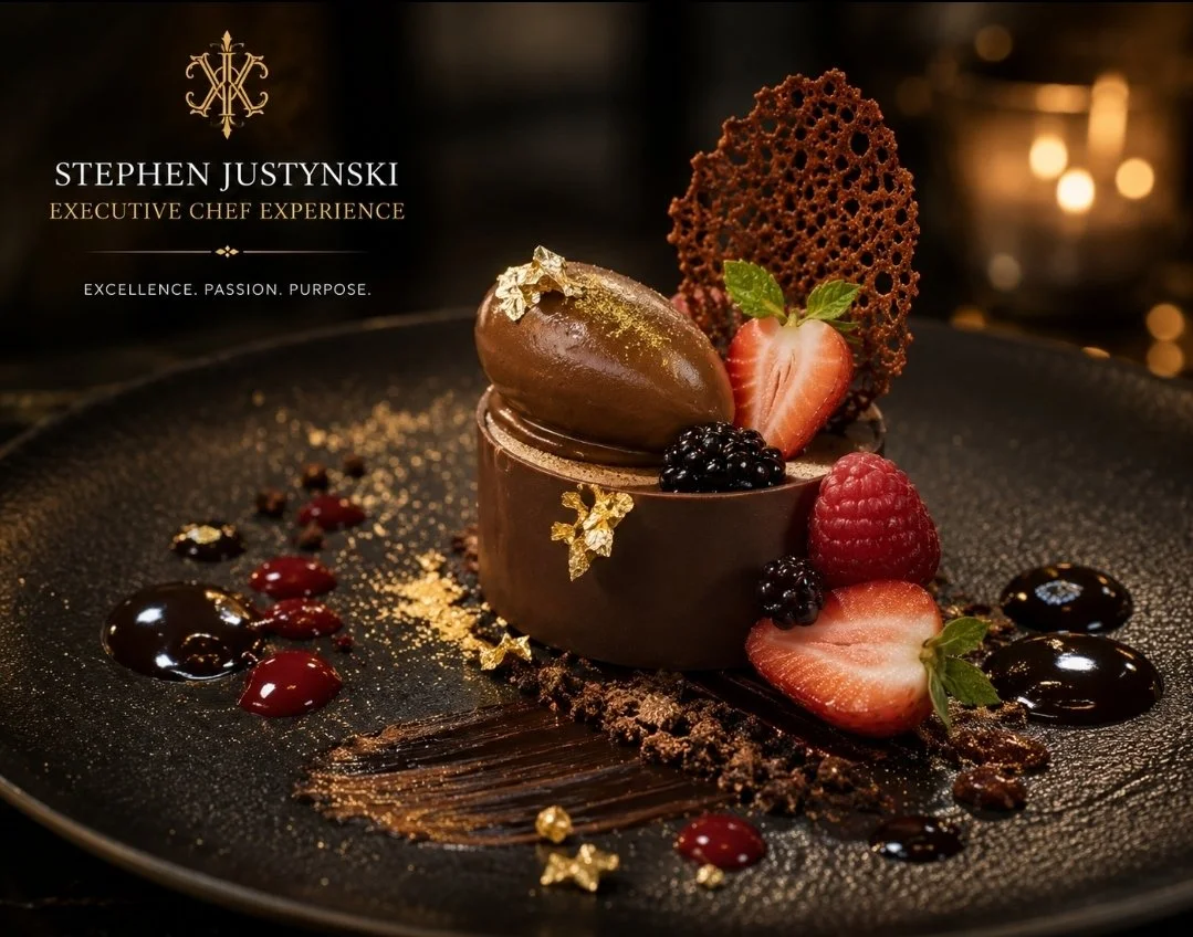 A gourmet chocolate dessert garnished with berries, fresh fruit, edible gold leaf, a decorative chocolate lattice, and artistic sauce drizzles on a black plate.