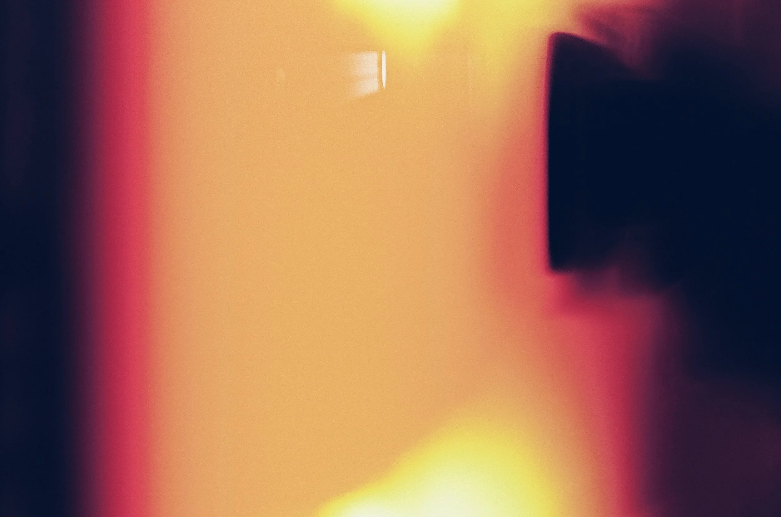 Abstract blurry image with warm tones of yellow, red, and dark purple, featuring indistinct shapes and no clear objects.