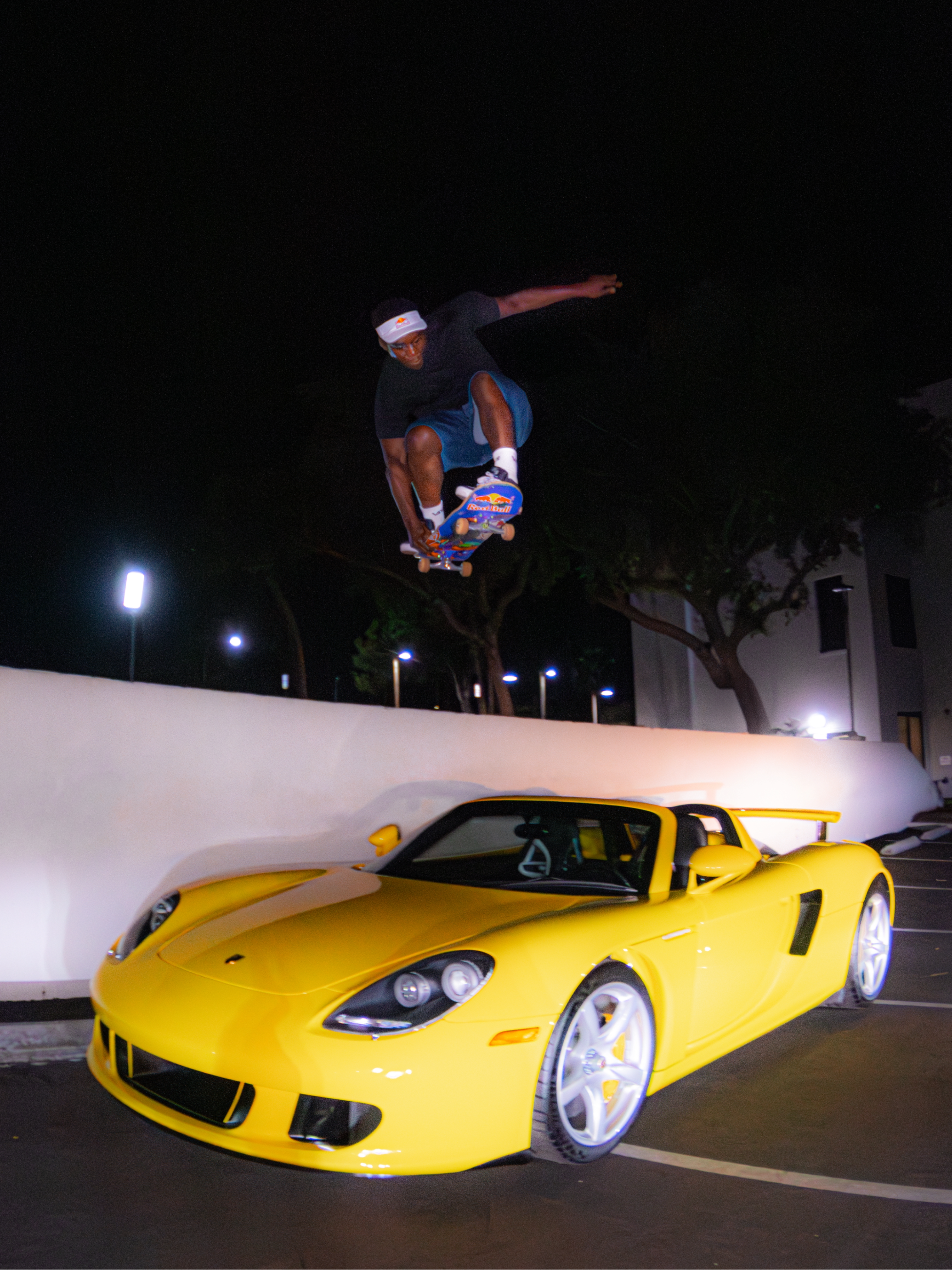 Nighttime scene of a person performing a stunt on a skateboard above a bright yellow sports car.
