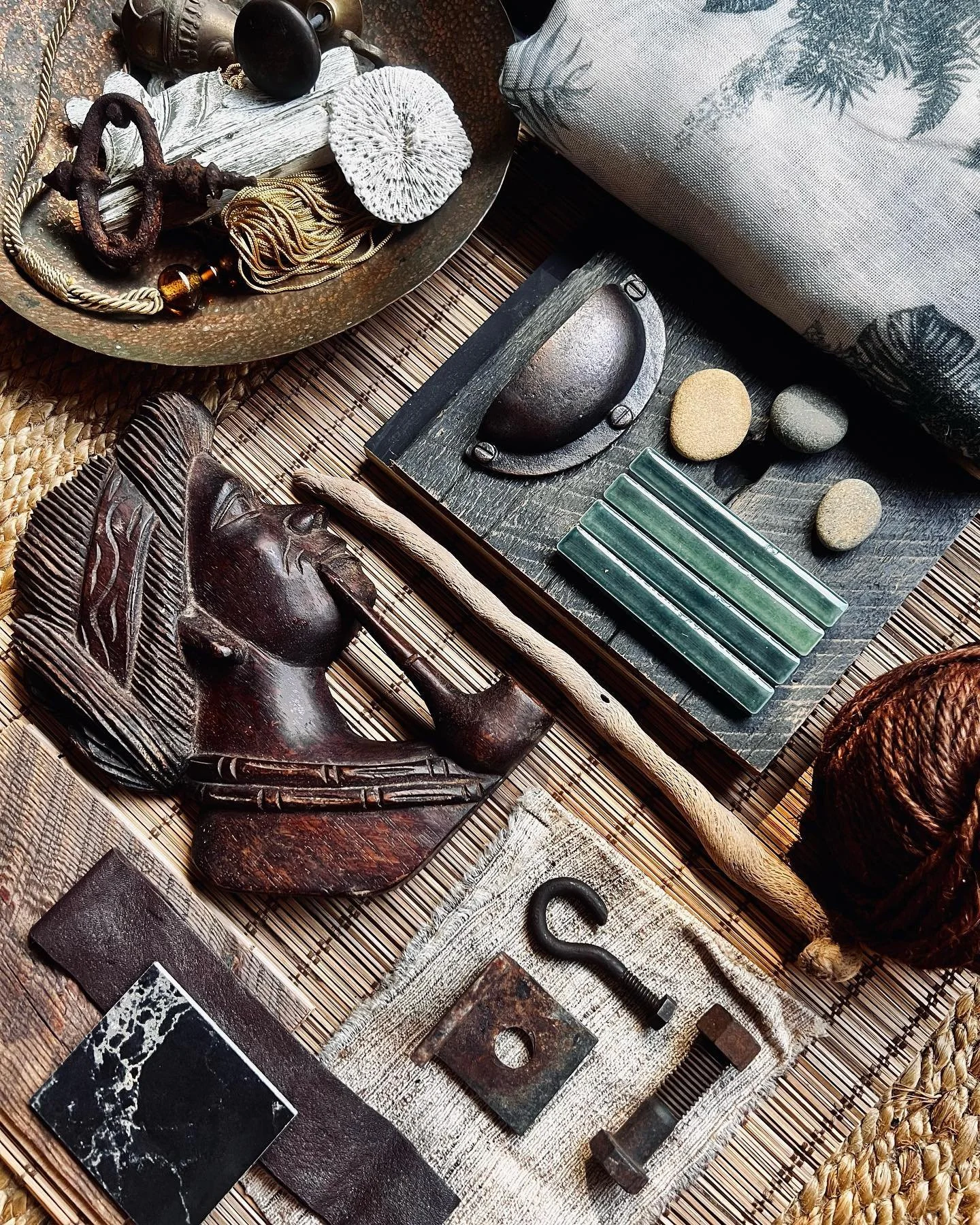 A collection of antique and tribal artifacts, including carved wooden masks, a snake-shaped figurine, stones, shells, and various decorative objects, arranged on a woven mat.