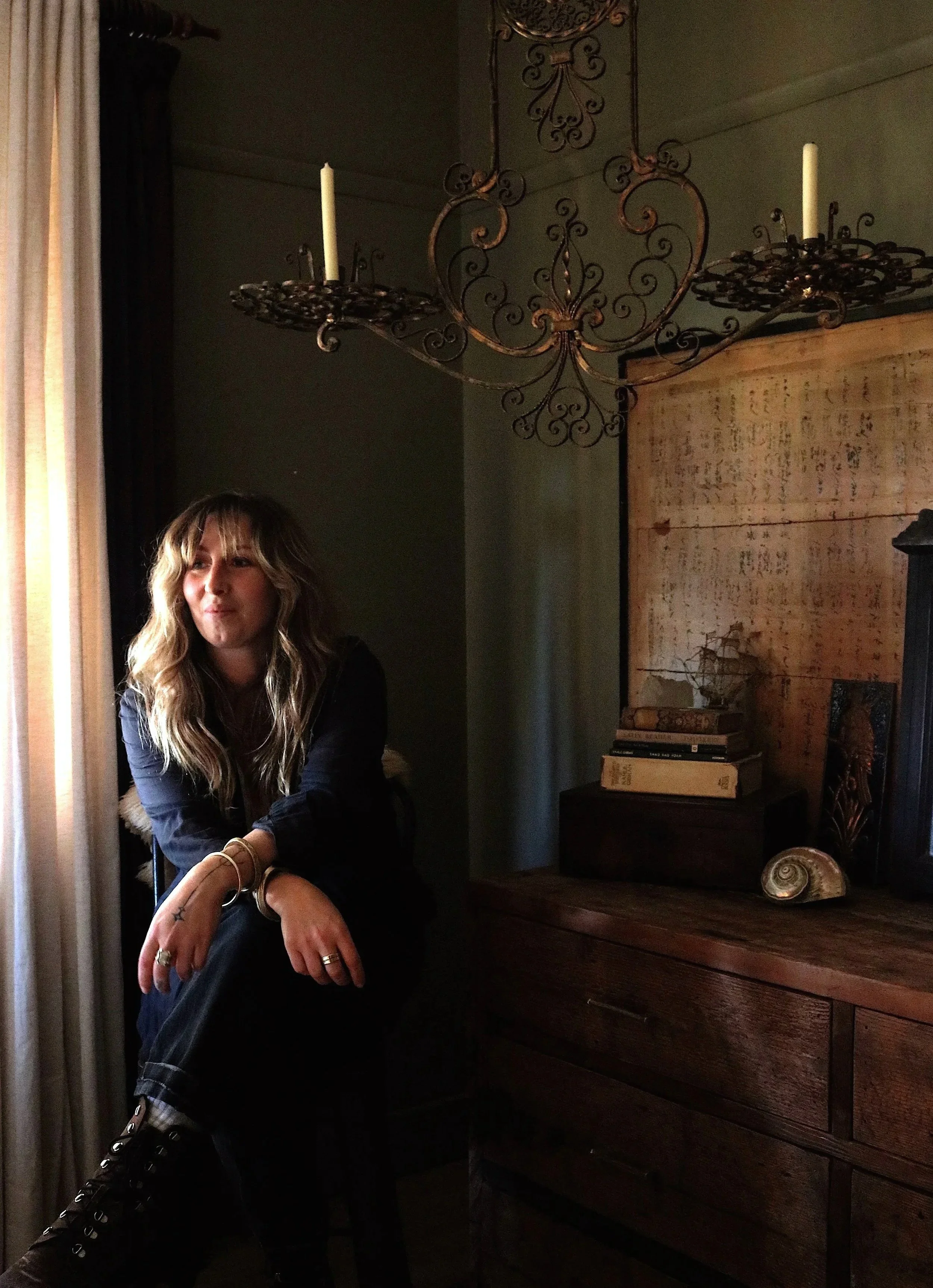Tara, founder of Fabled Spaces, seated in the dim candlelit interior of her home.