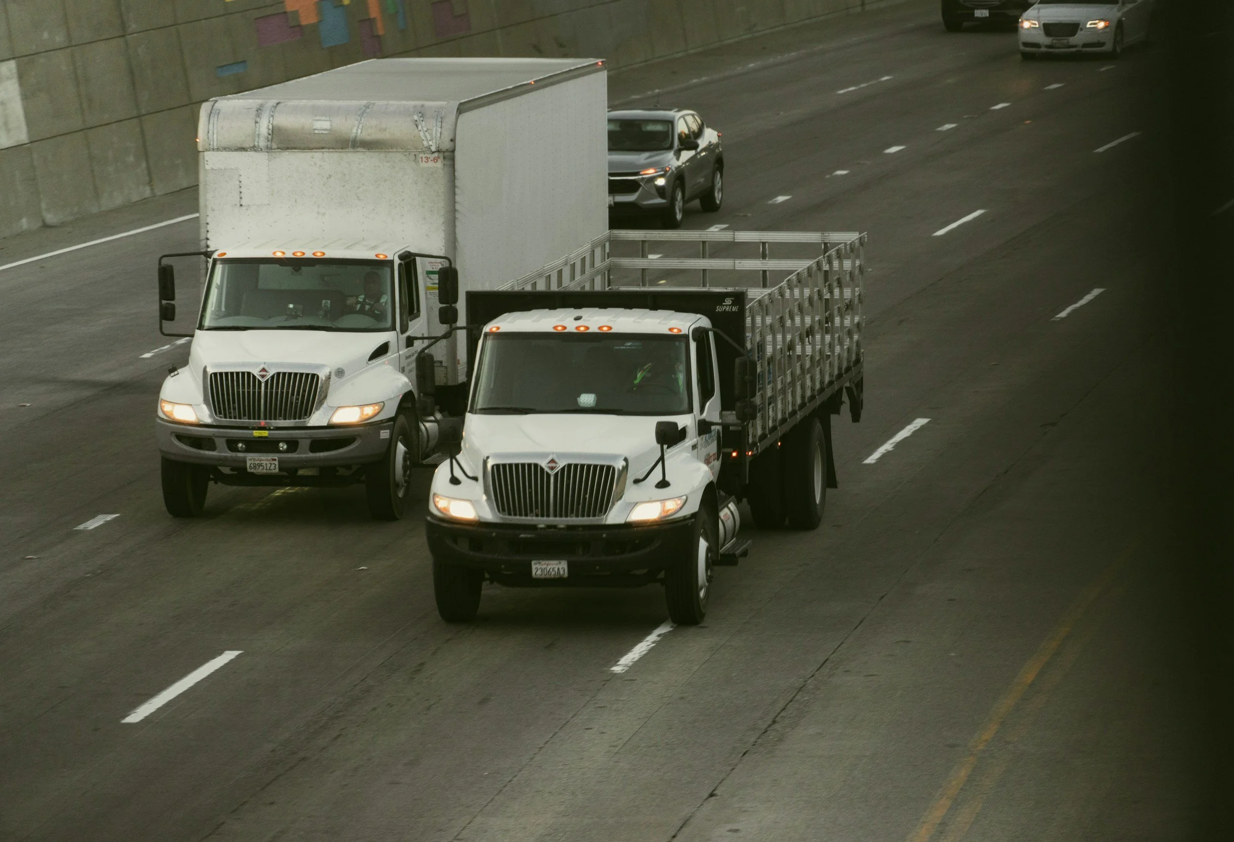 Multiple trucks and cars traveling on a highway tunnel with concrete walls and painted markings.