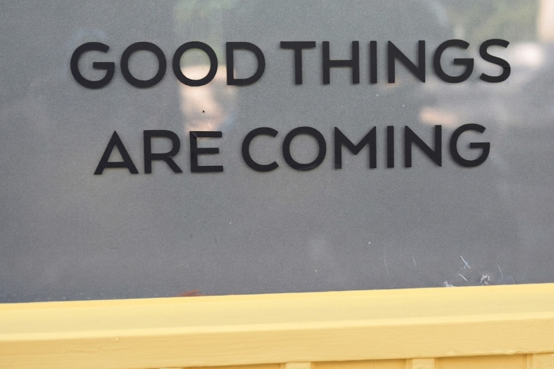 Sign with the words "Good Things Are Coming" against a gray background with reflections and a yellow border at the bottom.
