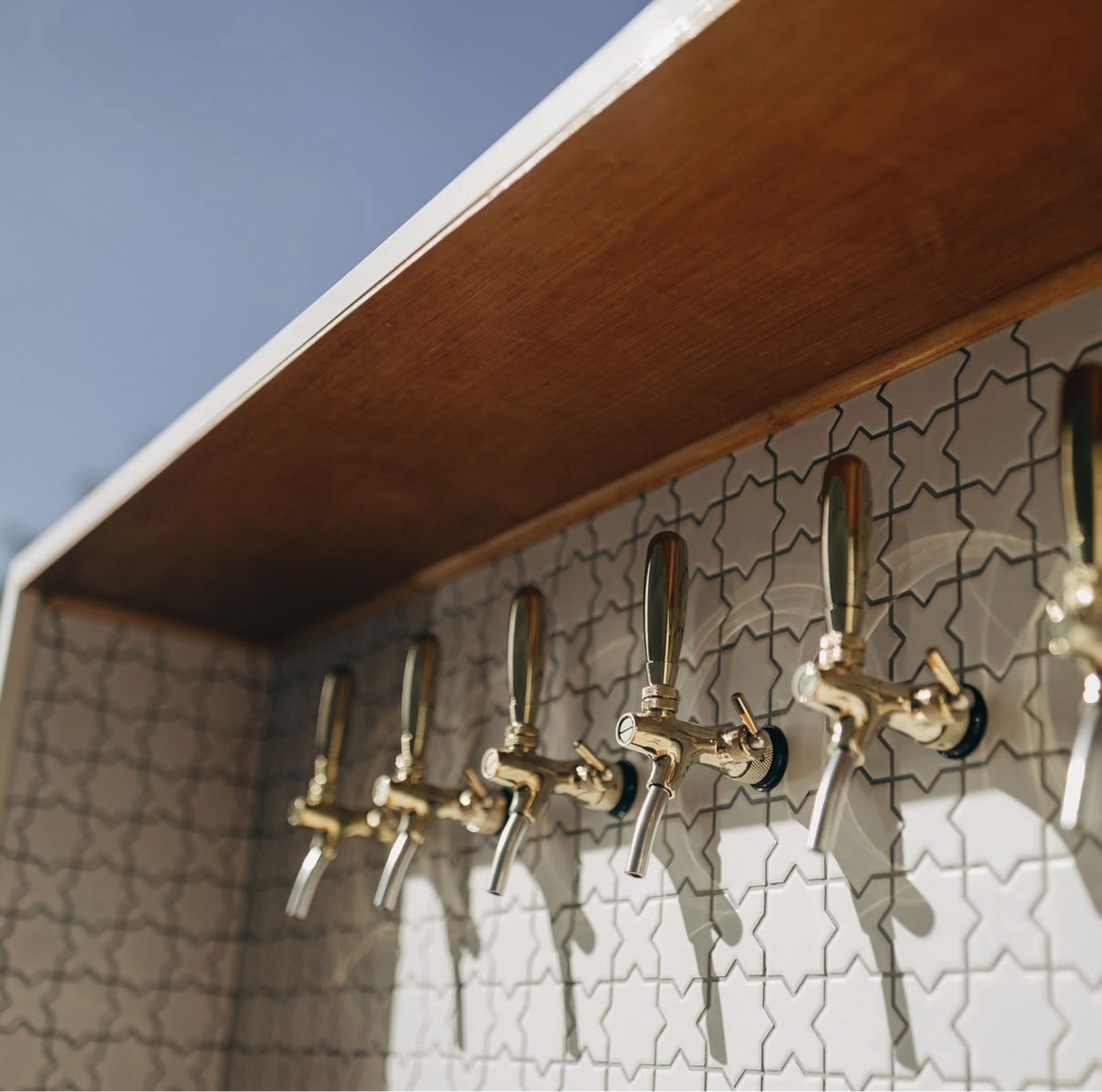 Close-up of a metal beer tap handle mounted on a textured wall with a geometric pattern.