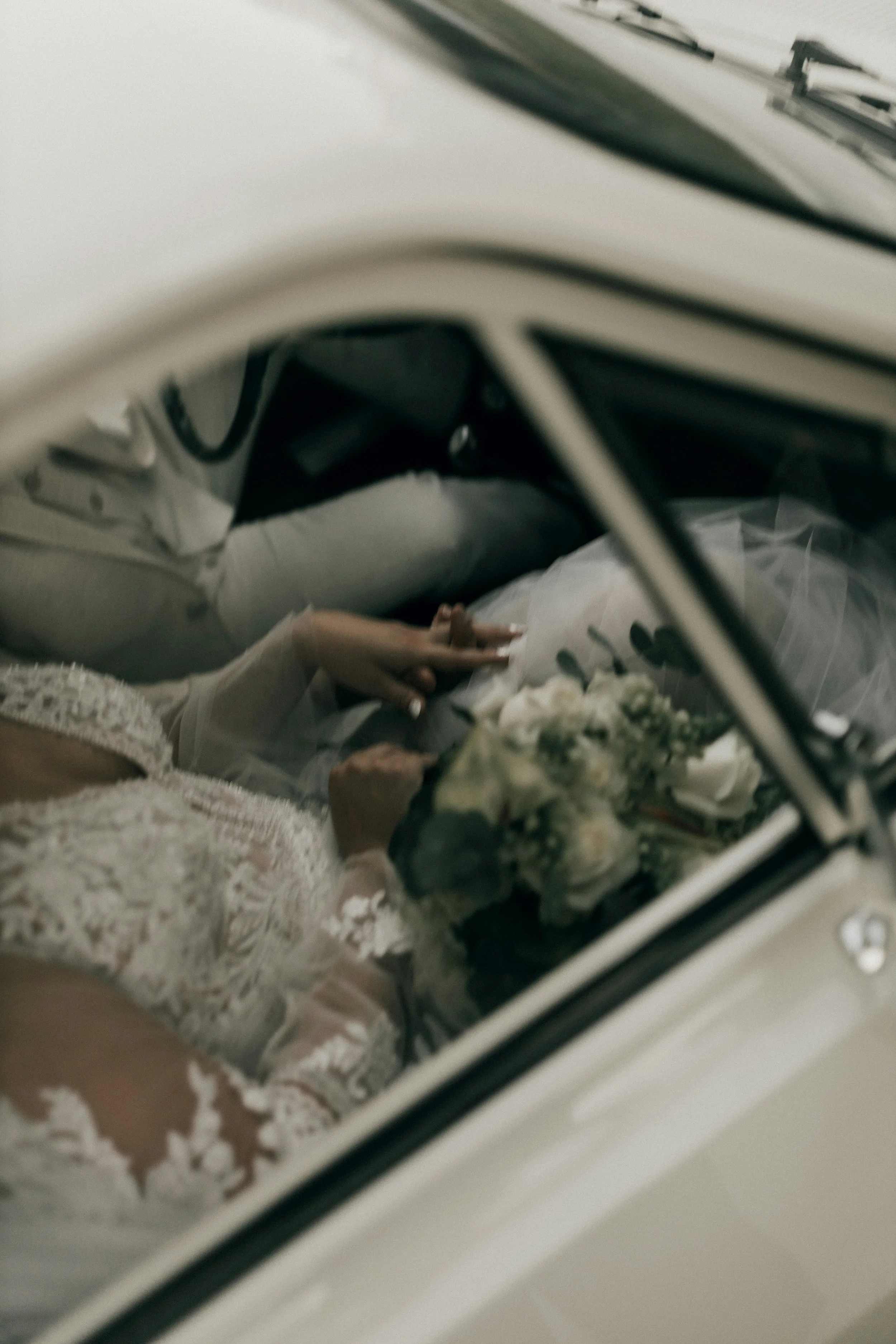 A small bouquet of white flowers with greenery lying near a white lace cloth, seen through the reflection of a mirror in a possibly bedroom or vanity setting.