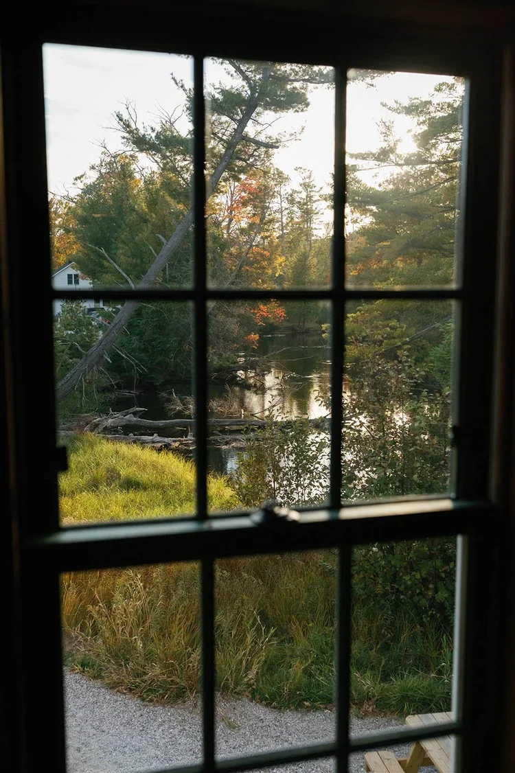 View of a wooded landscape with a river, trees, and a house through a window with individual panes in America.