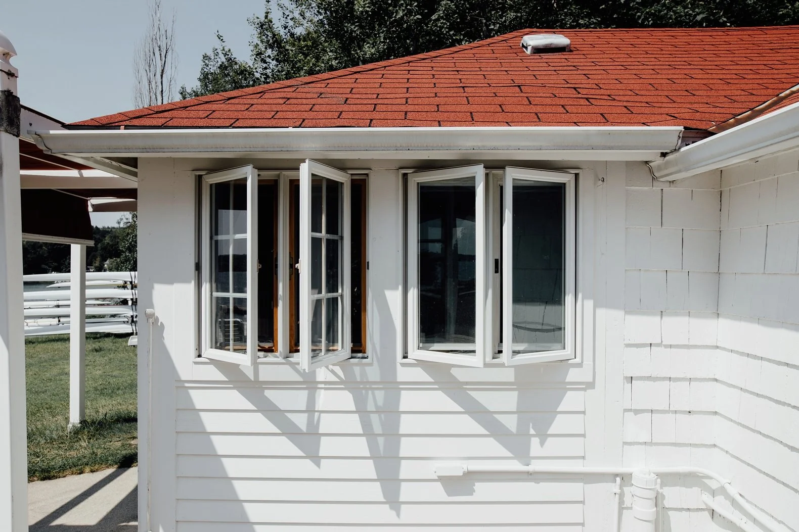 White house exterior with three large open window panels, a red shingle roof, and a white gutter system.