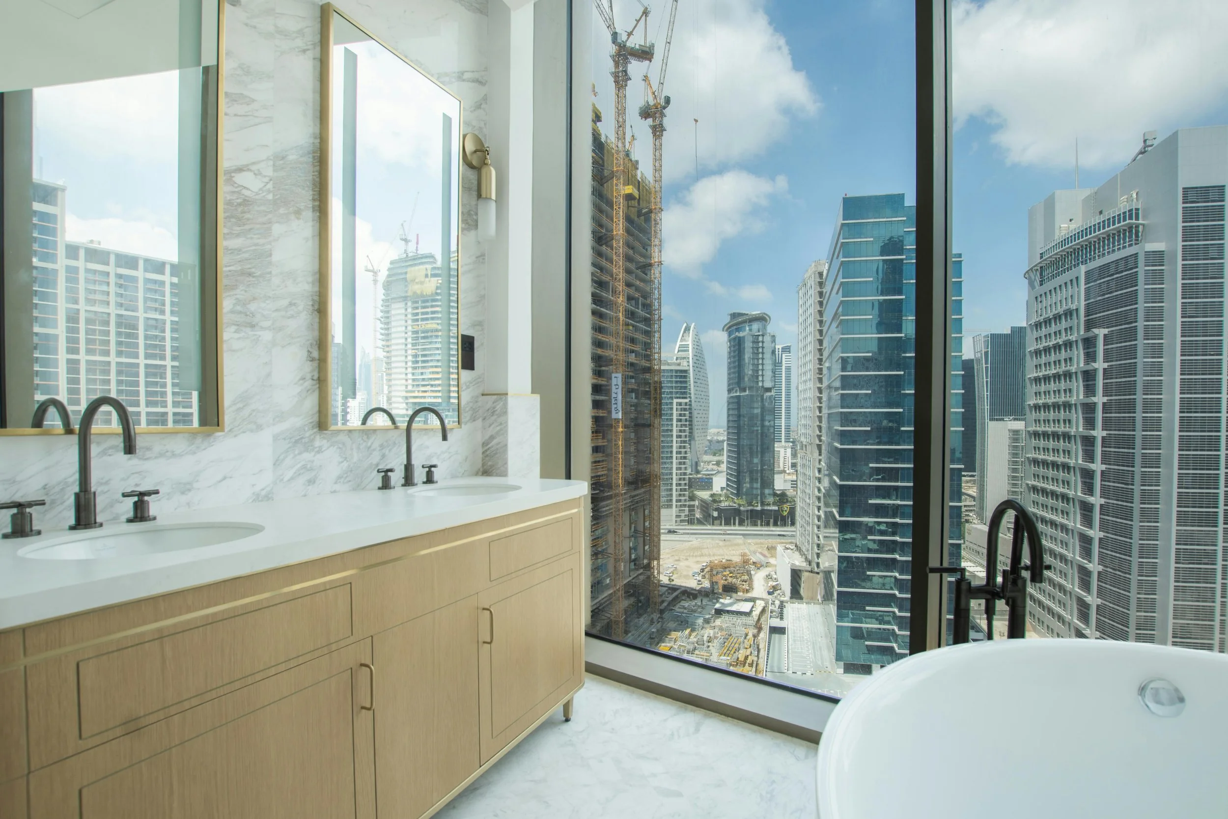 A modern bathroom with a large window showing an urban cityscape with tall buildings and construction cranes.