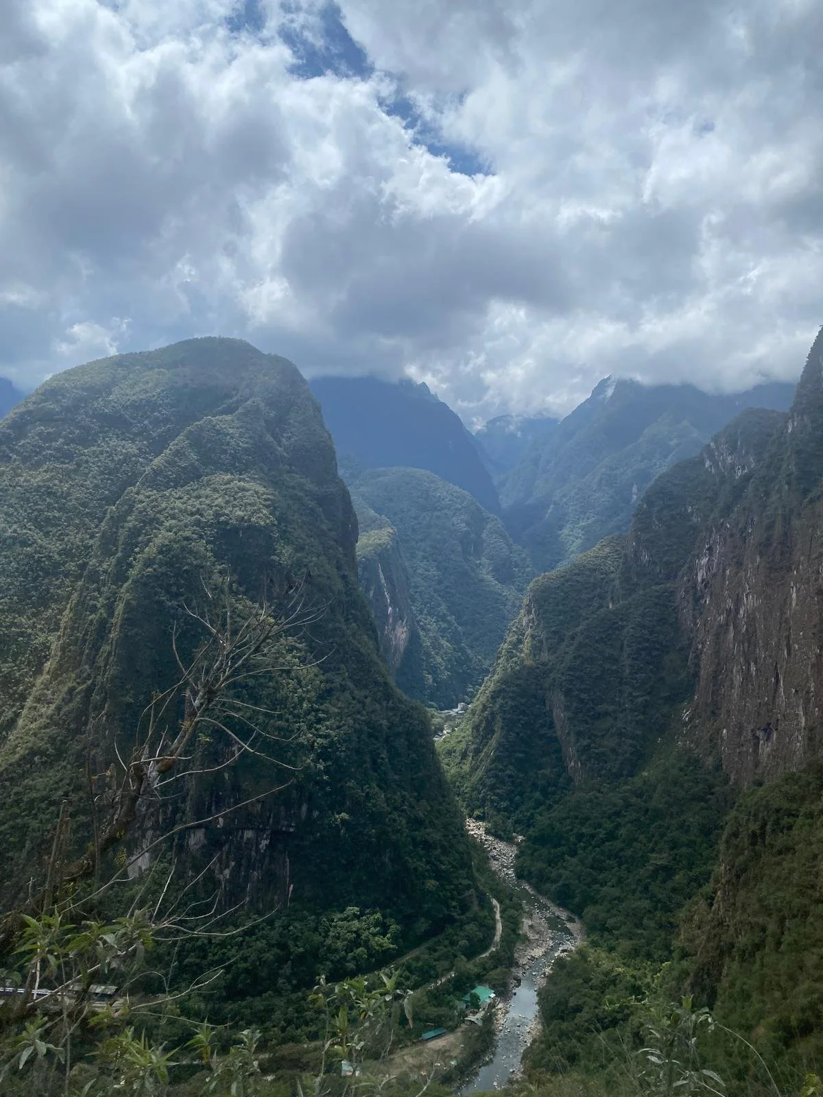 Mountain landscape with lush green valleys, a river flowing through, and cloudy sky.