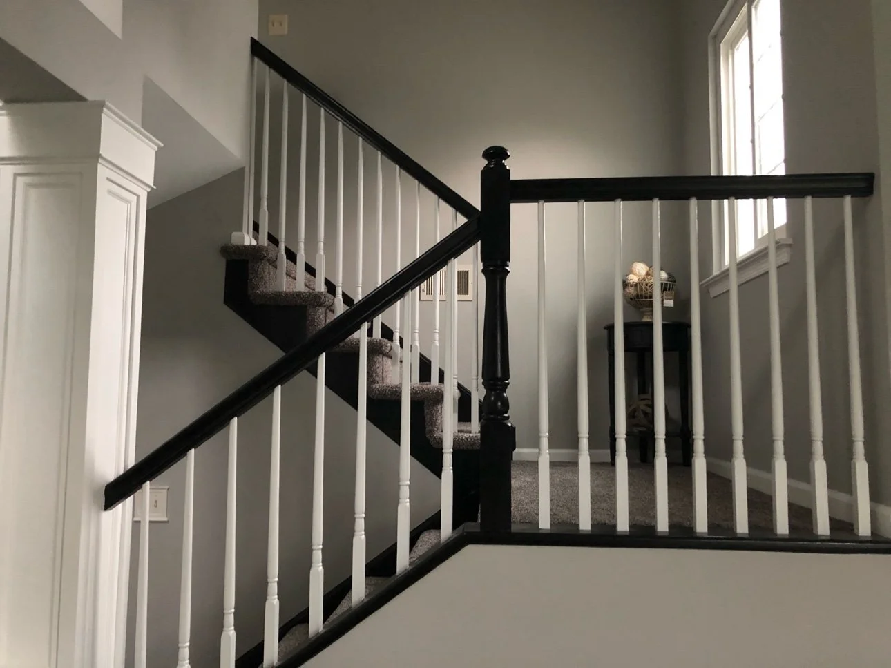 Staircase with black handrail and newel post, white balusters and gray walls