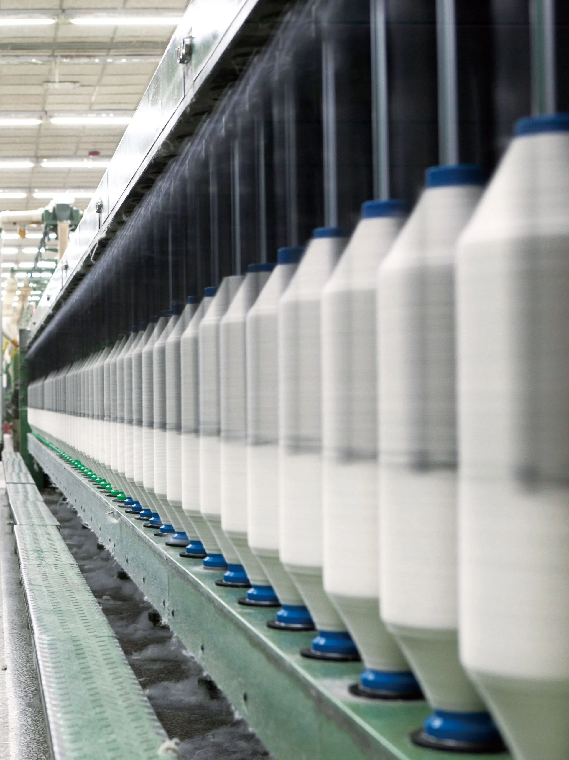 UCHINO yarn making towel factory. A row of white plastic bottles with blue caps on a conveyor belt in a factory or manufacturing plant.