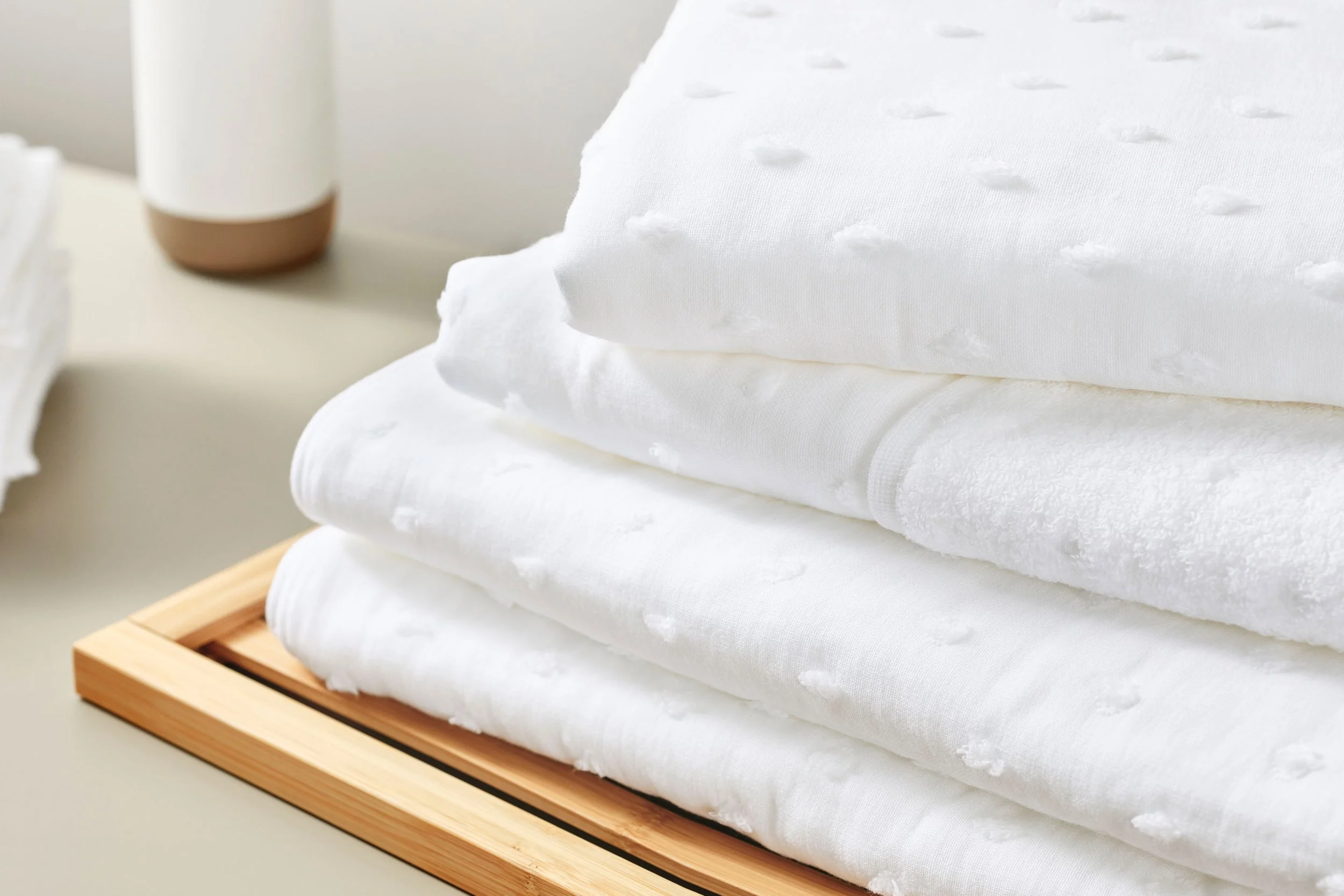 UCHINO Zero Twist Gauze Dot Towel. Stacked white towels with dotted texture on a wooden tray and a white and brown ceramic vase in the background.