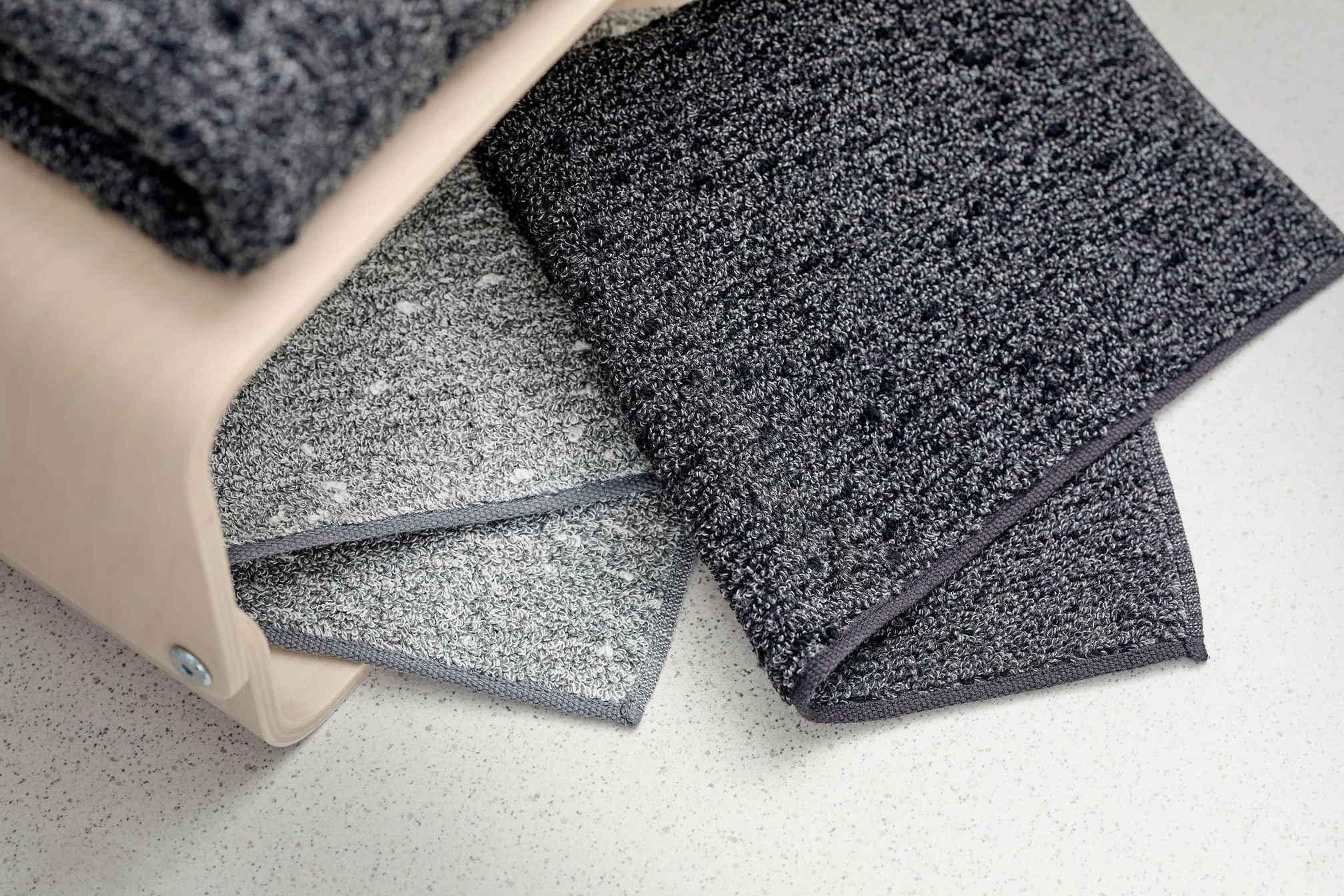 UCHINO Charcoal Towel. Black and Light Gray. Stack of gray and black fabric samples in a wooden storage box on a white countertop.