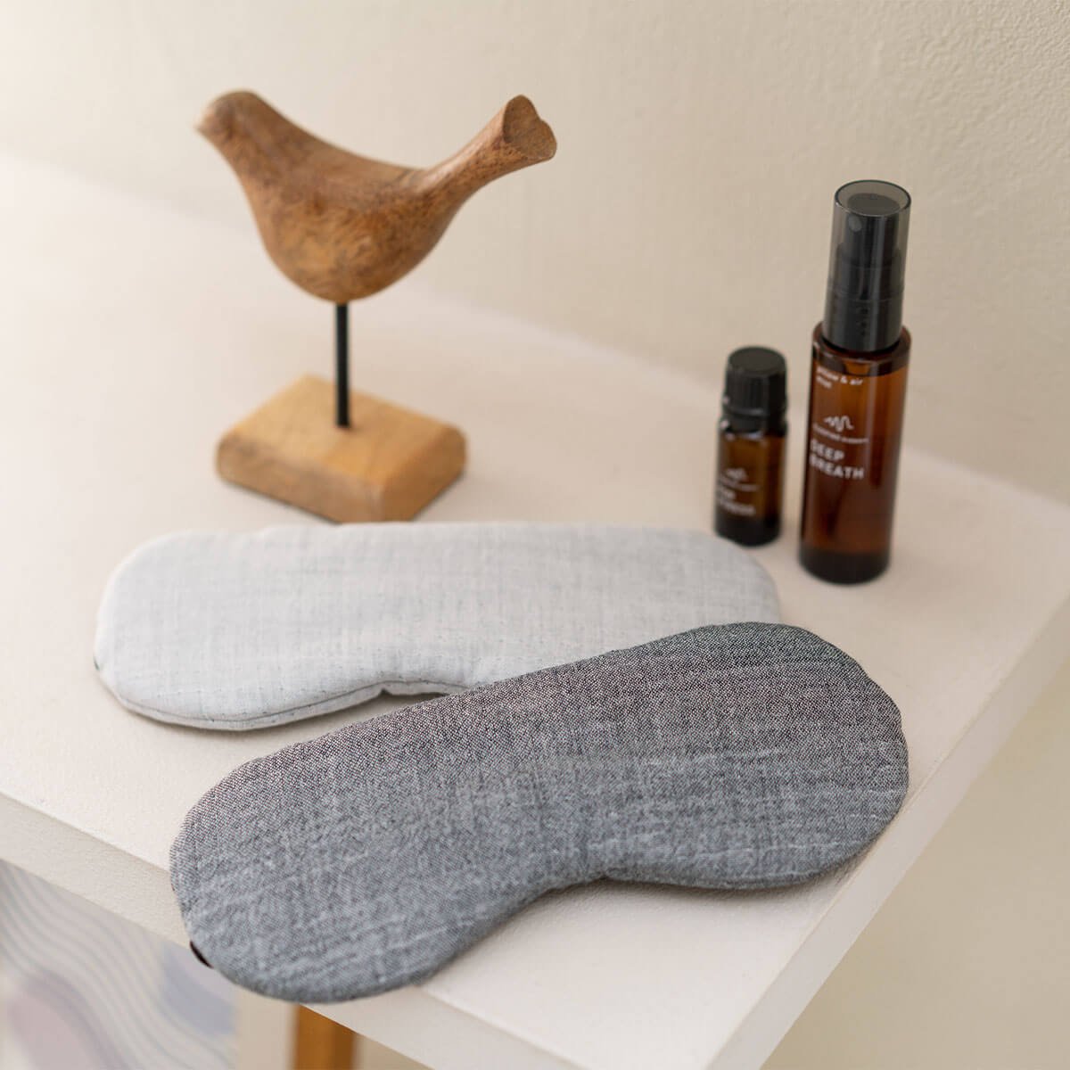A wooden bird sculpture, two bottles of essential oils, and two sleep masks on a white surface.