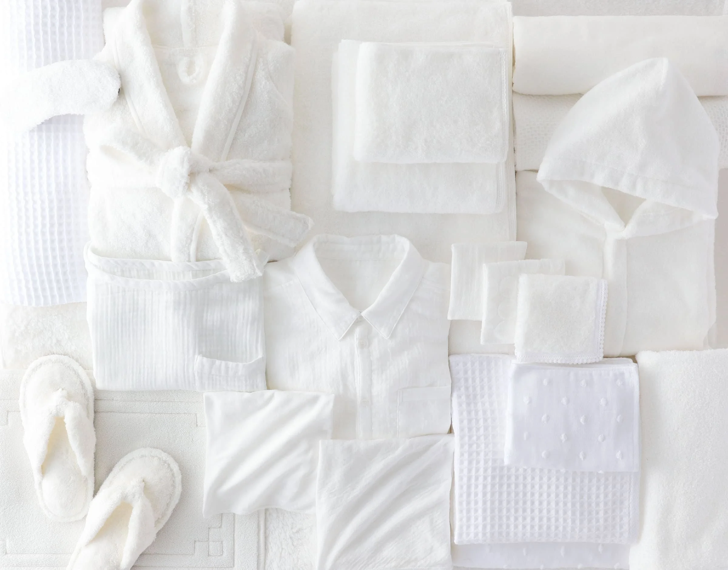 Various types of white medical gauze, bandages, and cotton pads arranged on a white surface.