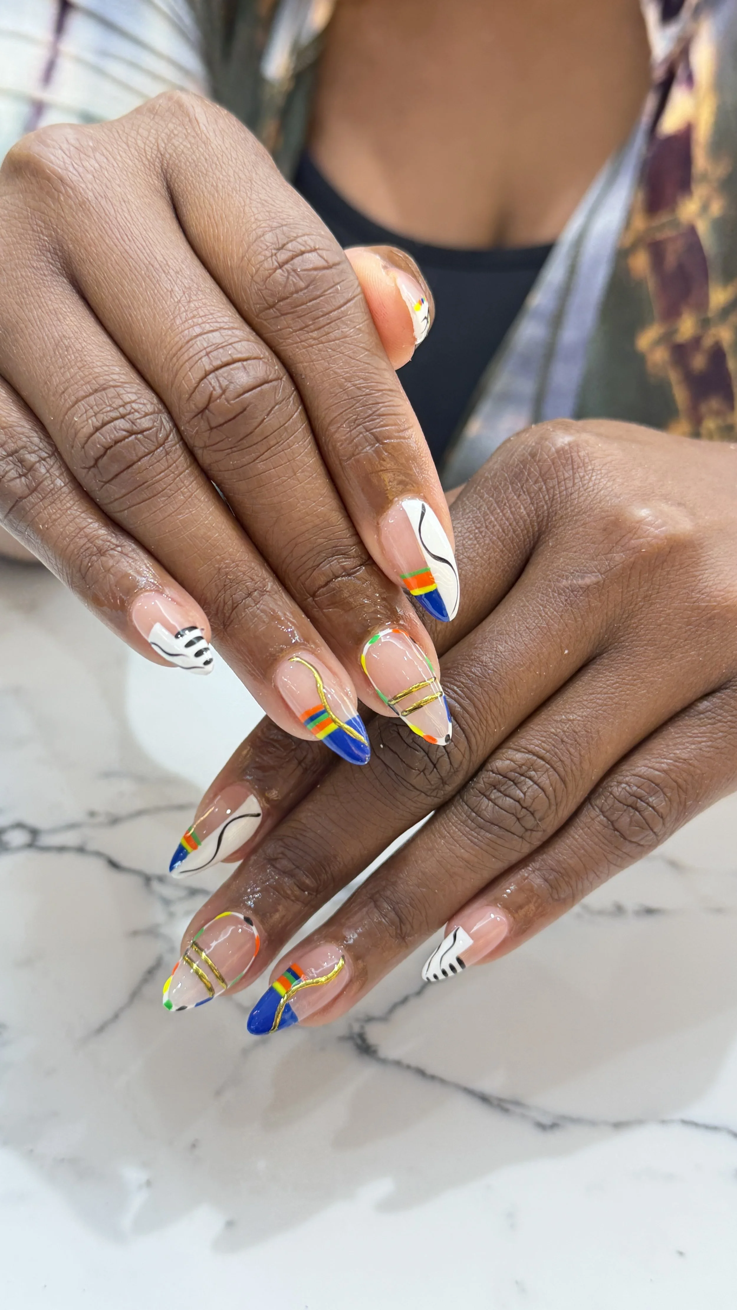 Colorful, artistic nail designs with stripes, curves, and various colors including blue, white, black, yellow, red, and green on long, almond-shaped nails.