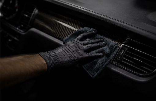 Person cleaning a car dashboard with a cloth, wearing black gloves.