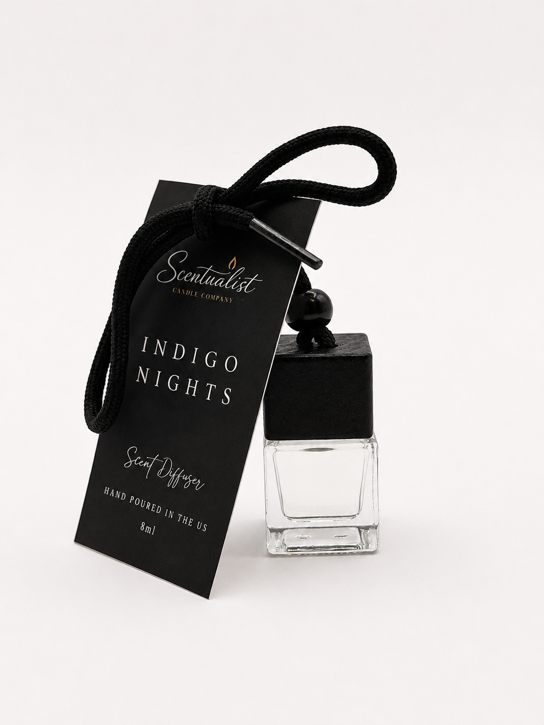A black and clear glass scent diffuser bottle labeled 'Indigo Nights' by Scentualist Candle Company with a black tag and wick holder, tied with a black rope.