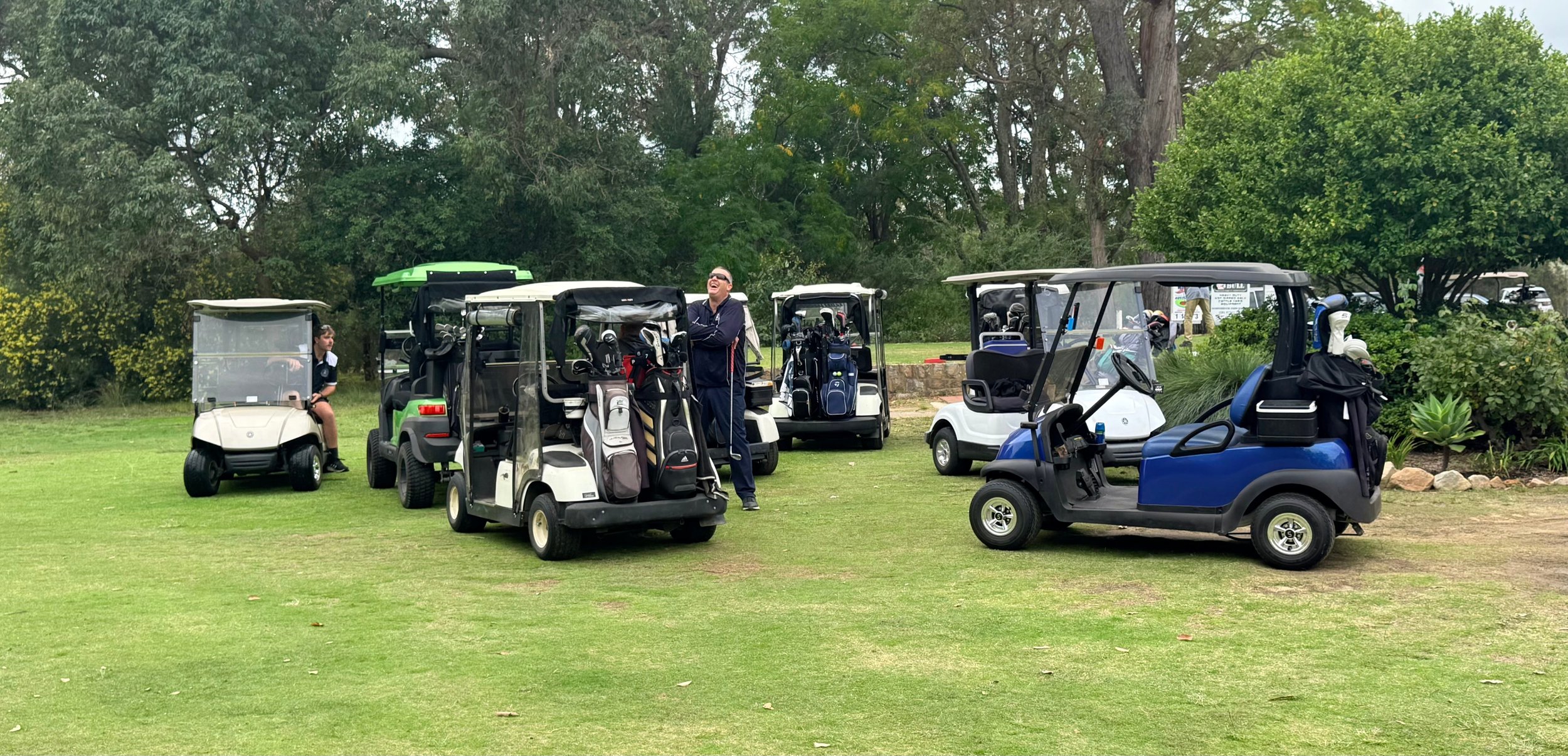 A group of golf carts parked on Donnybrook golf course, with a person standing near the carts and a child sitting in one of the carts, surrounded by greenery.