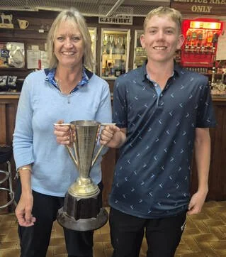 A woman and a young man standing in a store, holding a large silver trophy together.