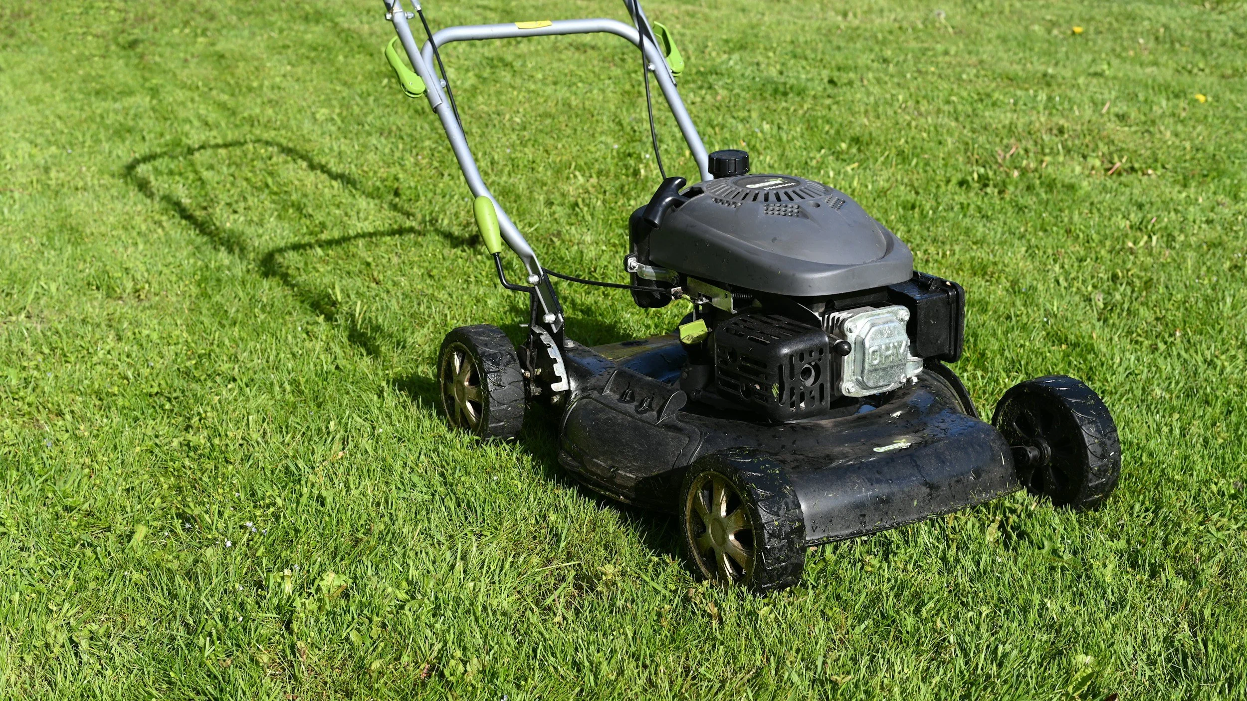 A black gas-powered lawn mower with a gray handle and green accents on a lush green lawn.