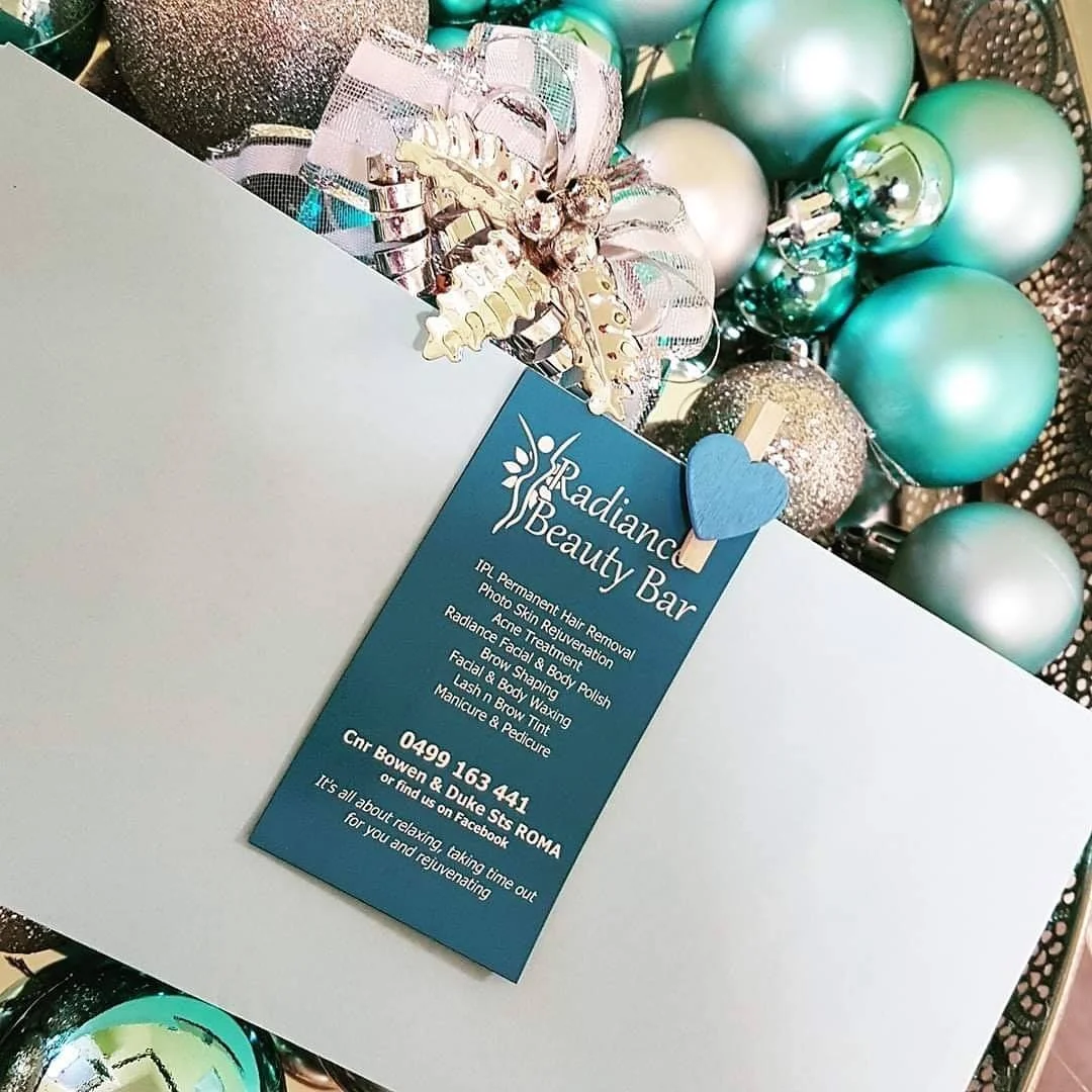 Business card for Radiance Beauty Bar placed on a white surface surrounded by teal, silver, and glittery Christmas ornaments and festive decorations.
