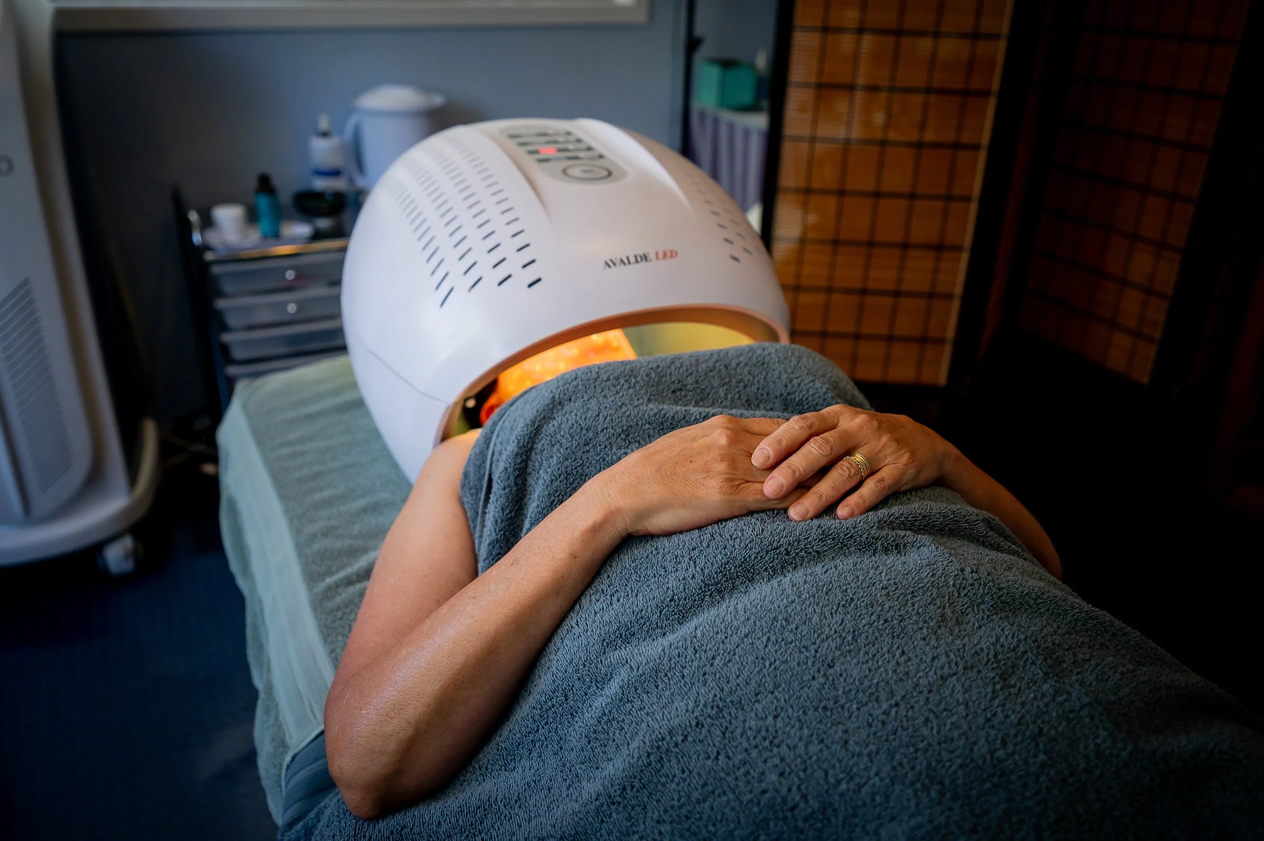 A person lying on a treatment bed with a hand on their abdomen during a phototherapy session using a white LED light device in a treatment room.