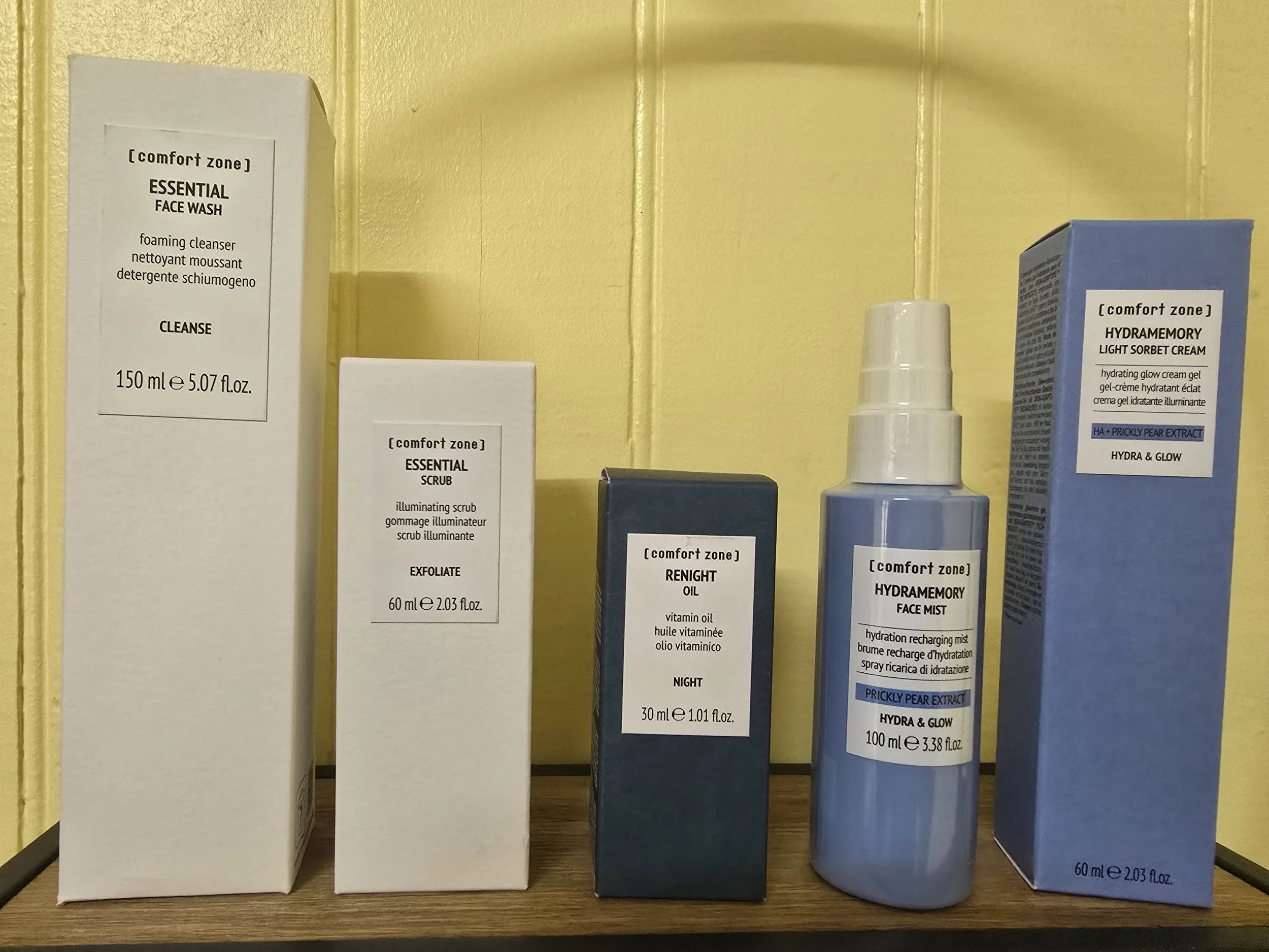 Boxes of skincare products with labels for face wash, scrub, night oil, and face mist on a yellow wall shelf.