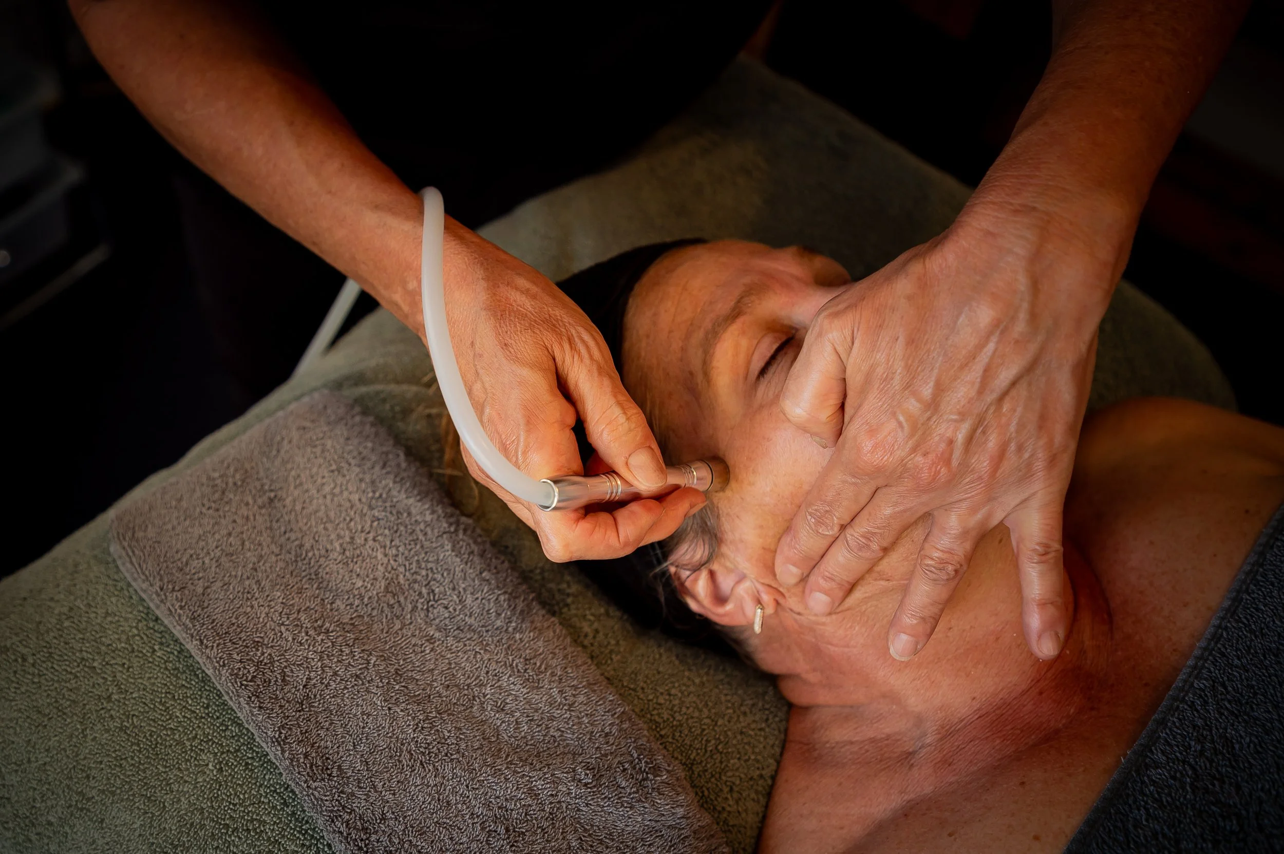 Person receiving a facial massage or treatment while lying on a massage table covered with a towel.