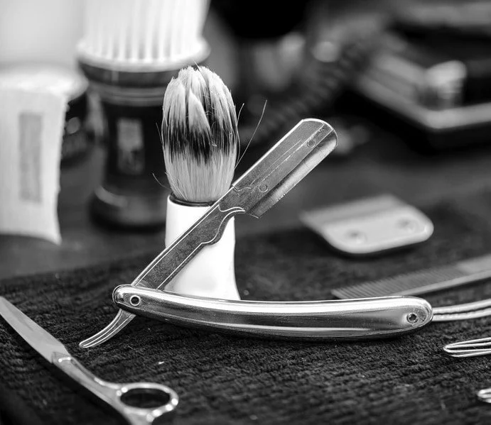 Barber's tools including a straight razor, shaving brush, and scissors on a black towel.