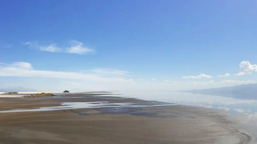At the shoreline of Lake Natron's vast, otherworldly landscape with flamingo in the far distance