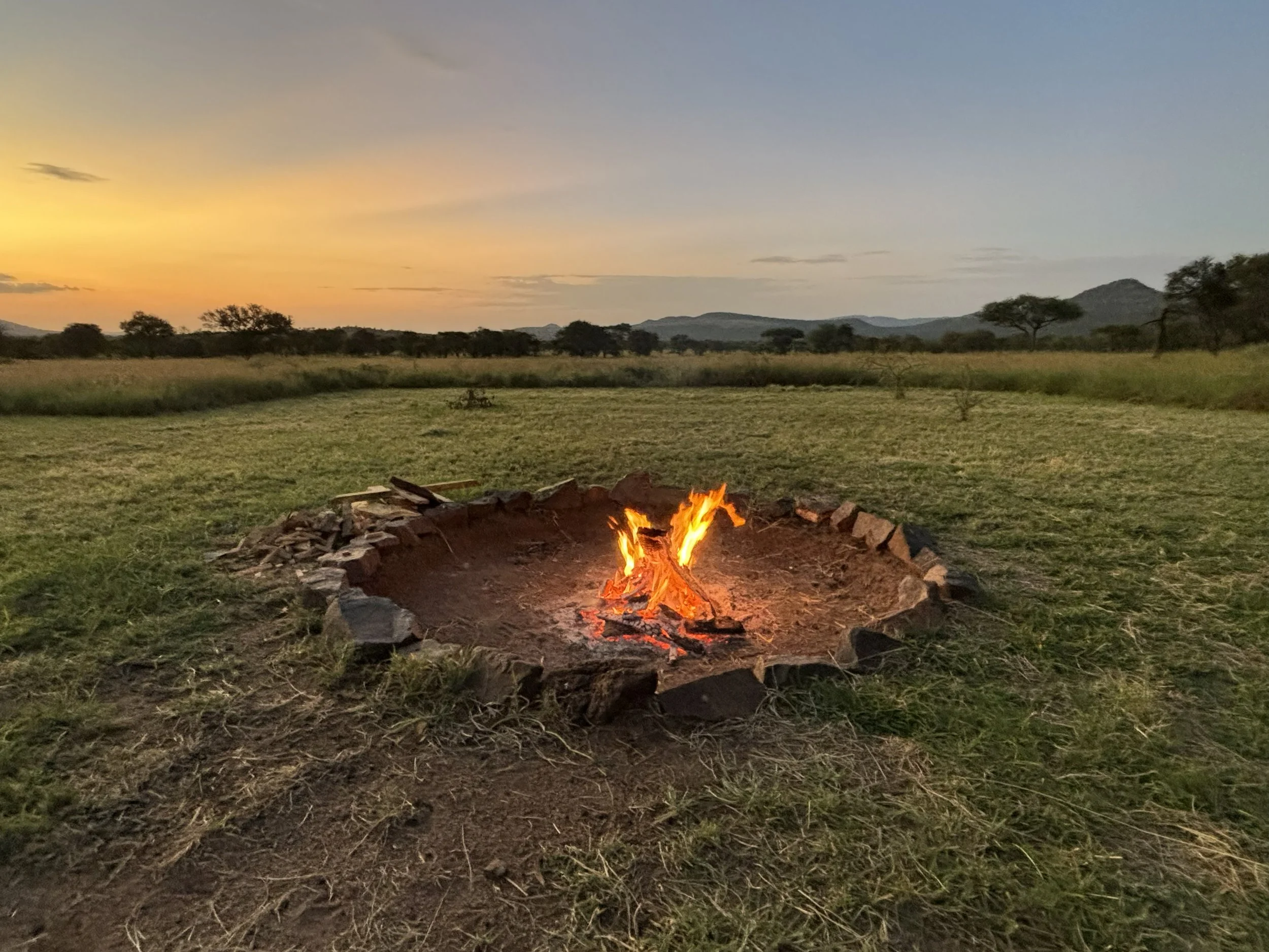 A warm campfire with flames surrounded by rocks, set in the Serengeti Plains, Tanzania during sunset