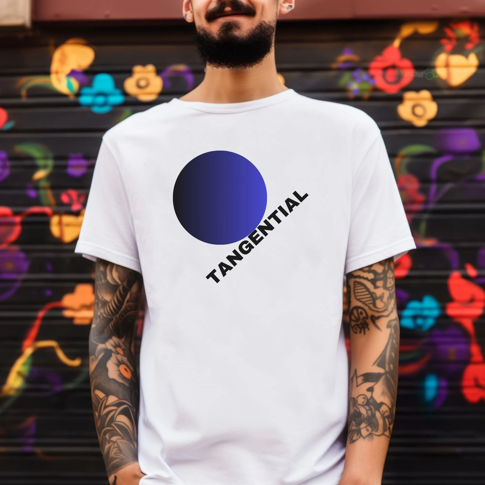 Close-up of a man with a mustache and beard wearing a white T-shirt with a large black circle and the word 'TANGENTIAL' printed on it, standing in front of a wall with colorful graffiti featuring various shapes and designs.
