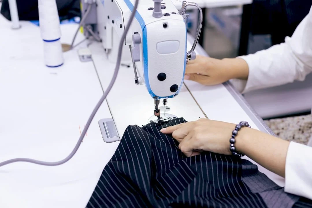 A person operating a sewing machine to stitch a dark pinstriped fabric.