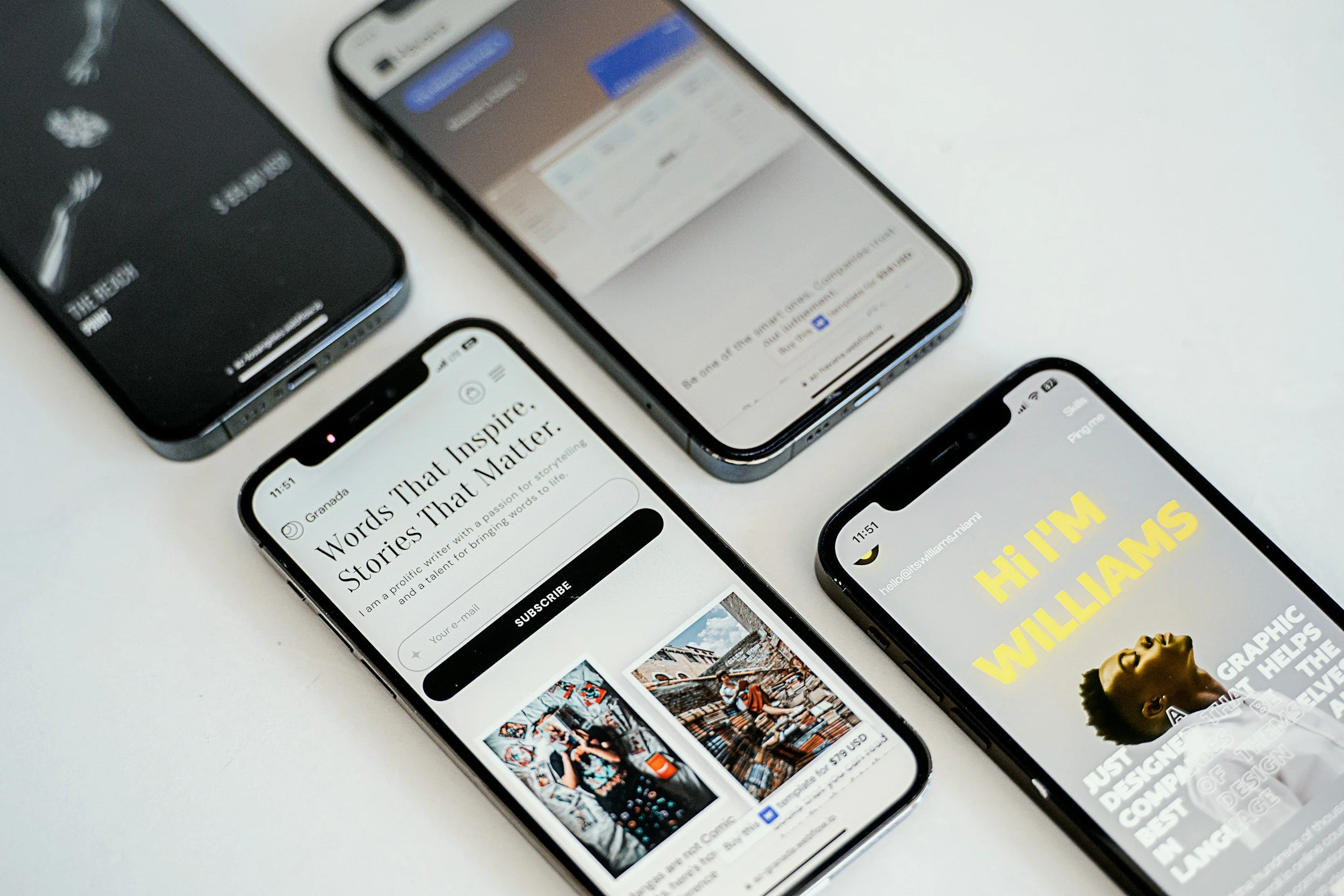 Several smartphones placed on a white surface, displaying websites and images.