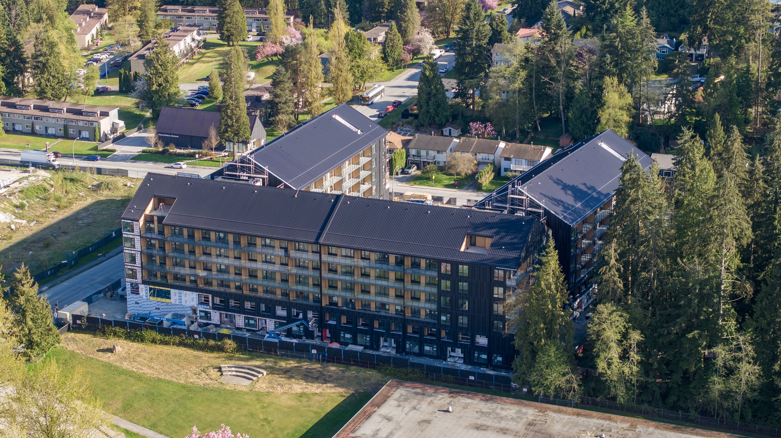 Aerial view of a residential neighborhood with new modern apartment buildings under construction, surrounded by green trees and a mix of single-family homes.