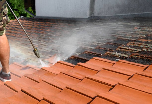 Person pressure washing a clay tile roof.