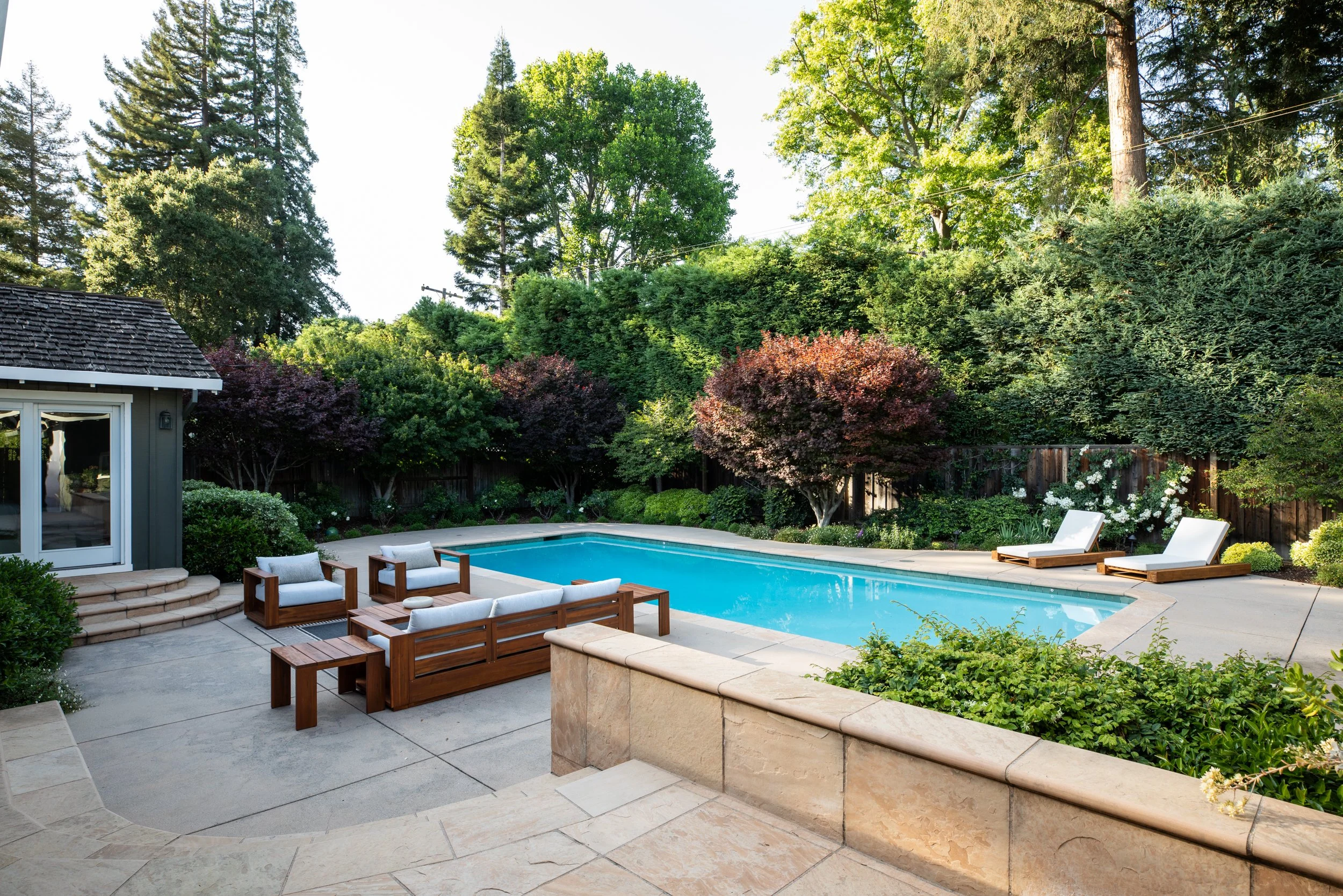 Backyard with swimming pool, outdoor furniture, trees, and shrubs.