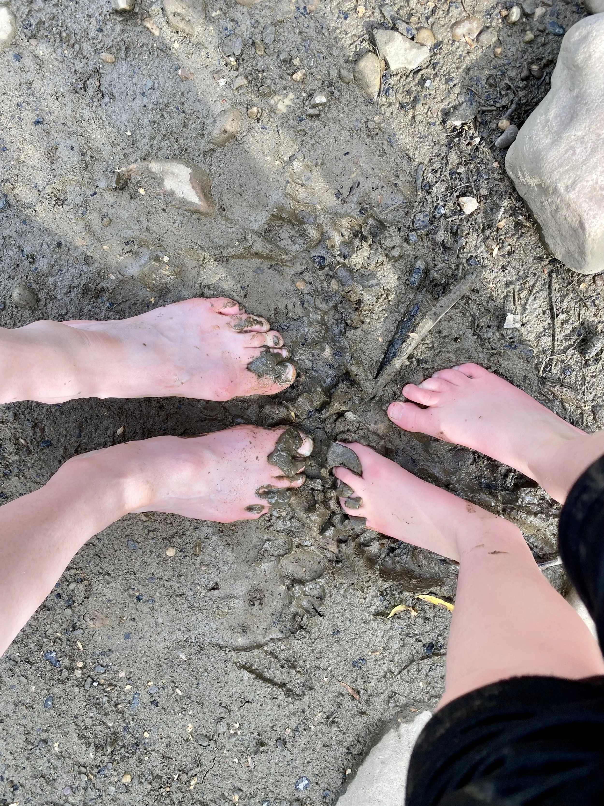 Close-up photo of bare feet on muddy ground, with distinct footprints and rocks visible.