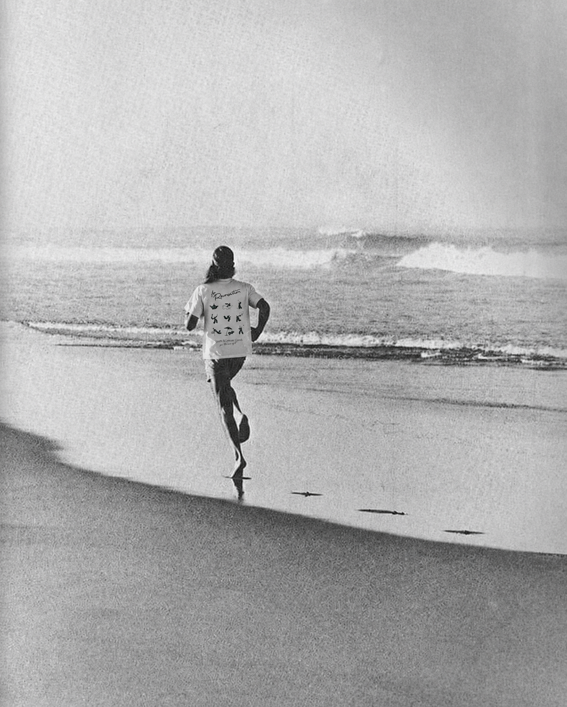 A person jogging on the beach near the shoreline, with waves in the background, in black and white.